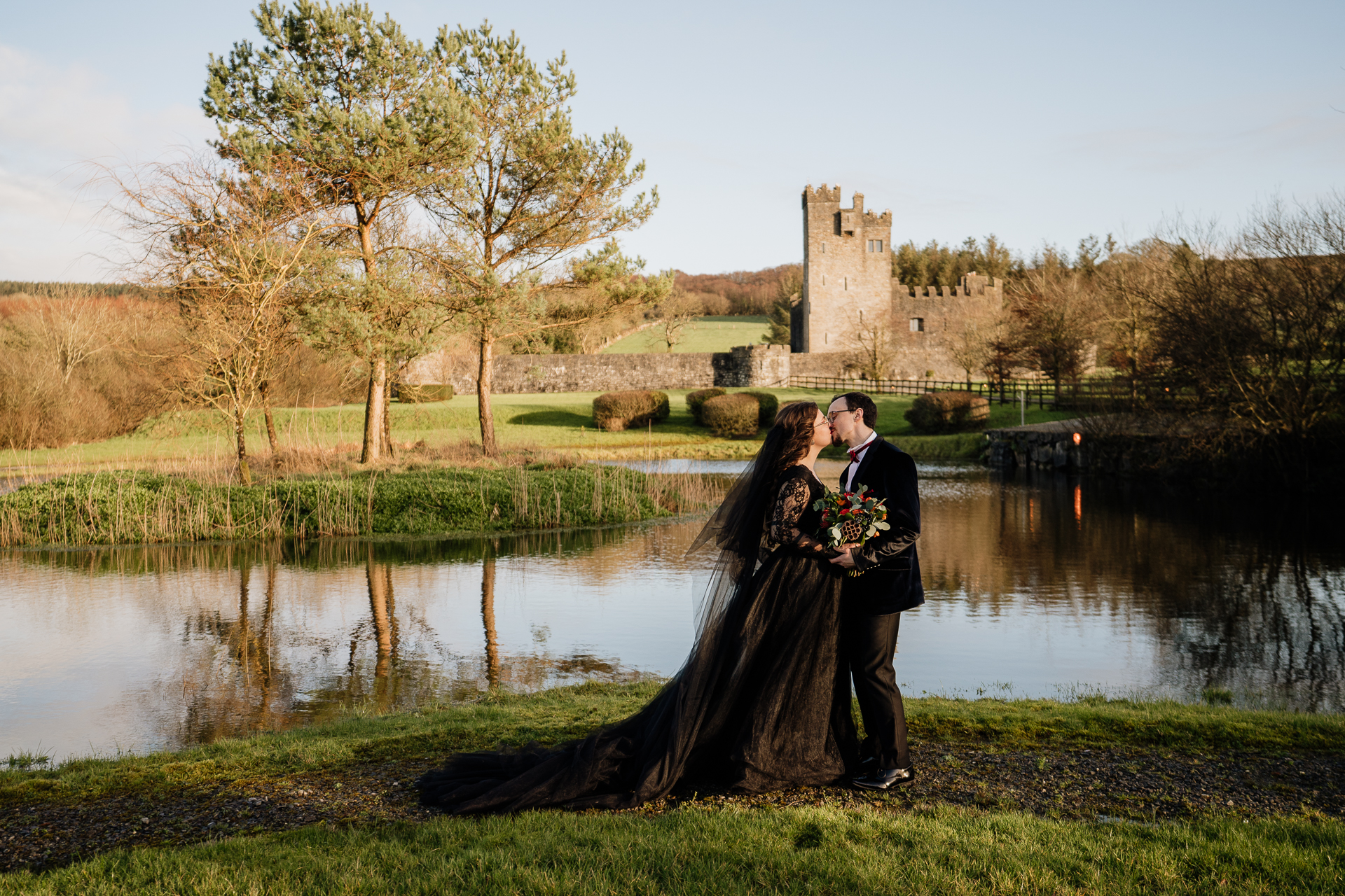 A man and woman kissing by a pond with a castle in the background