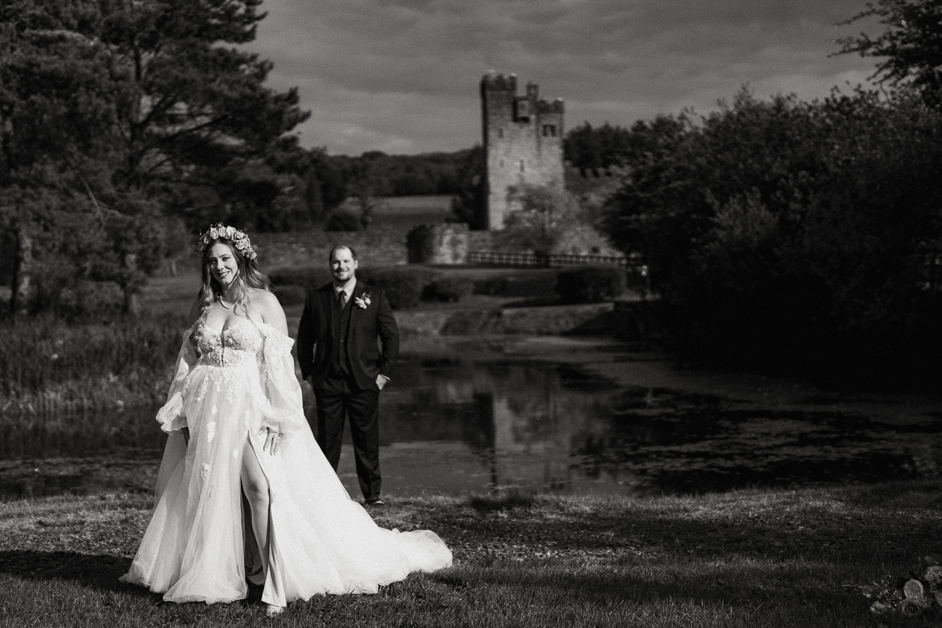 A bride and groom walking down a path by a pond