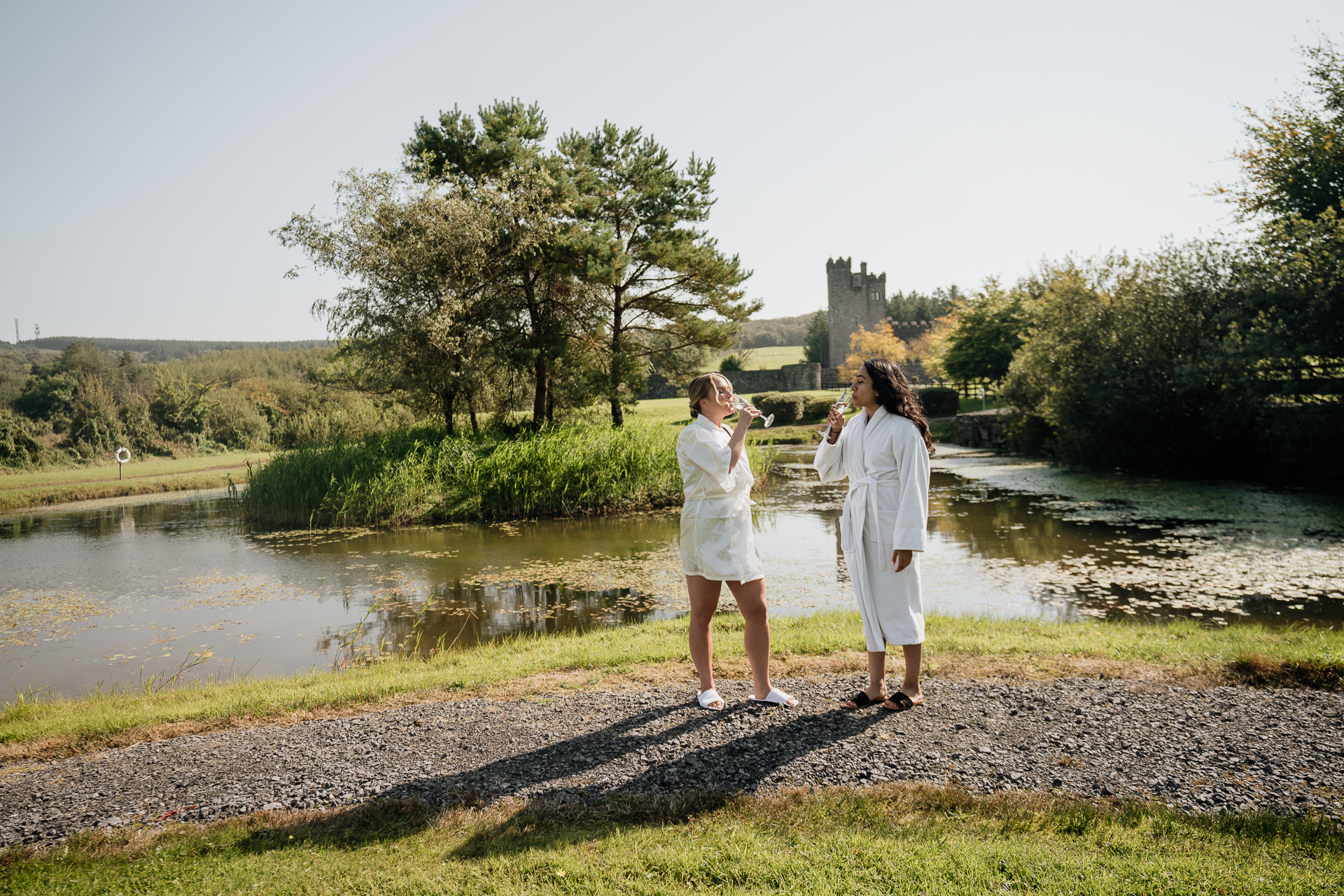 A couple of women in white robes standing by a pond with trees