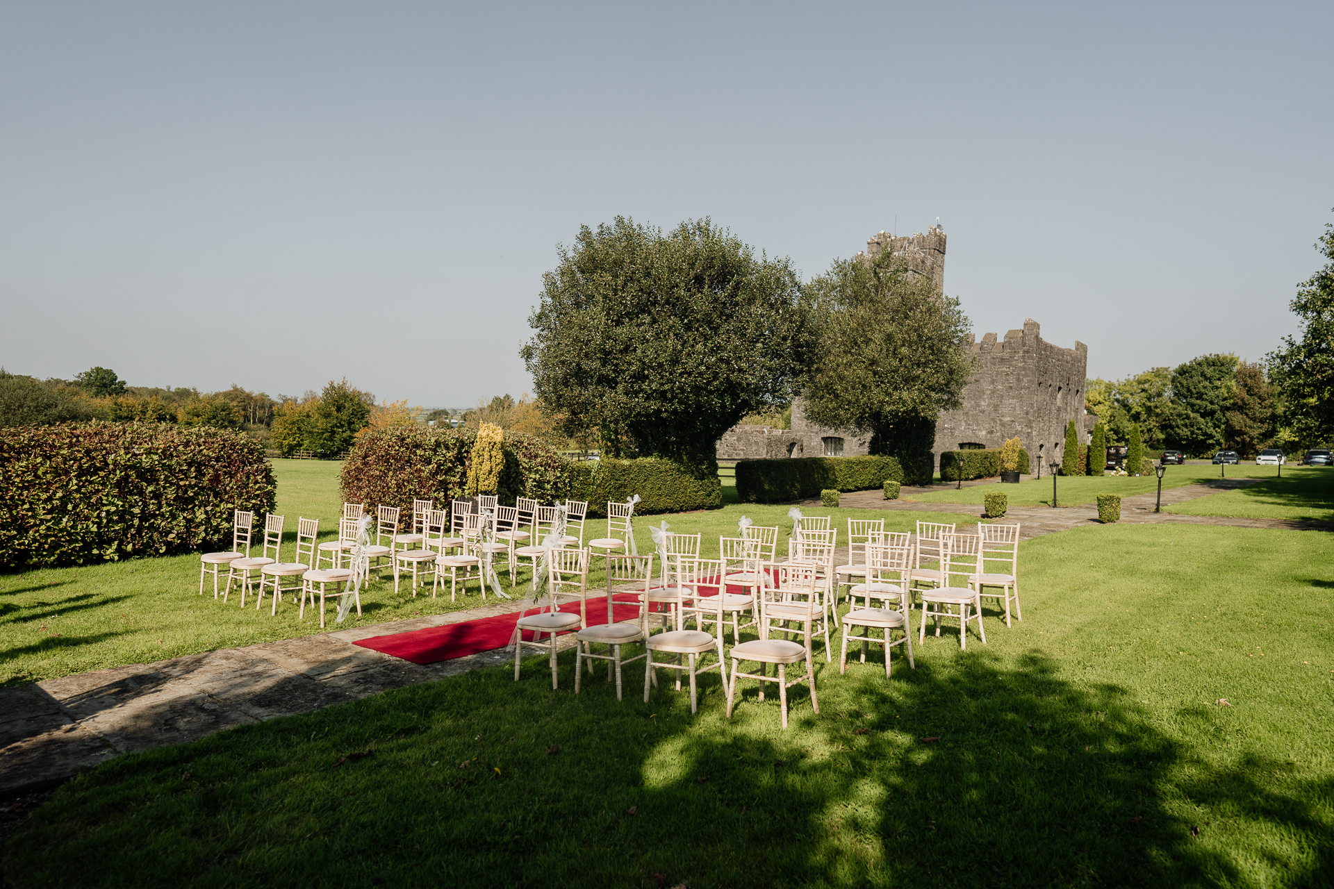 A row of white chairs in a grassy field with trees and a castle in the background