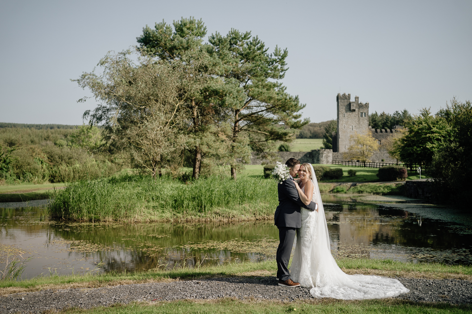 A man and woman kissing by a river with a castle in the background