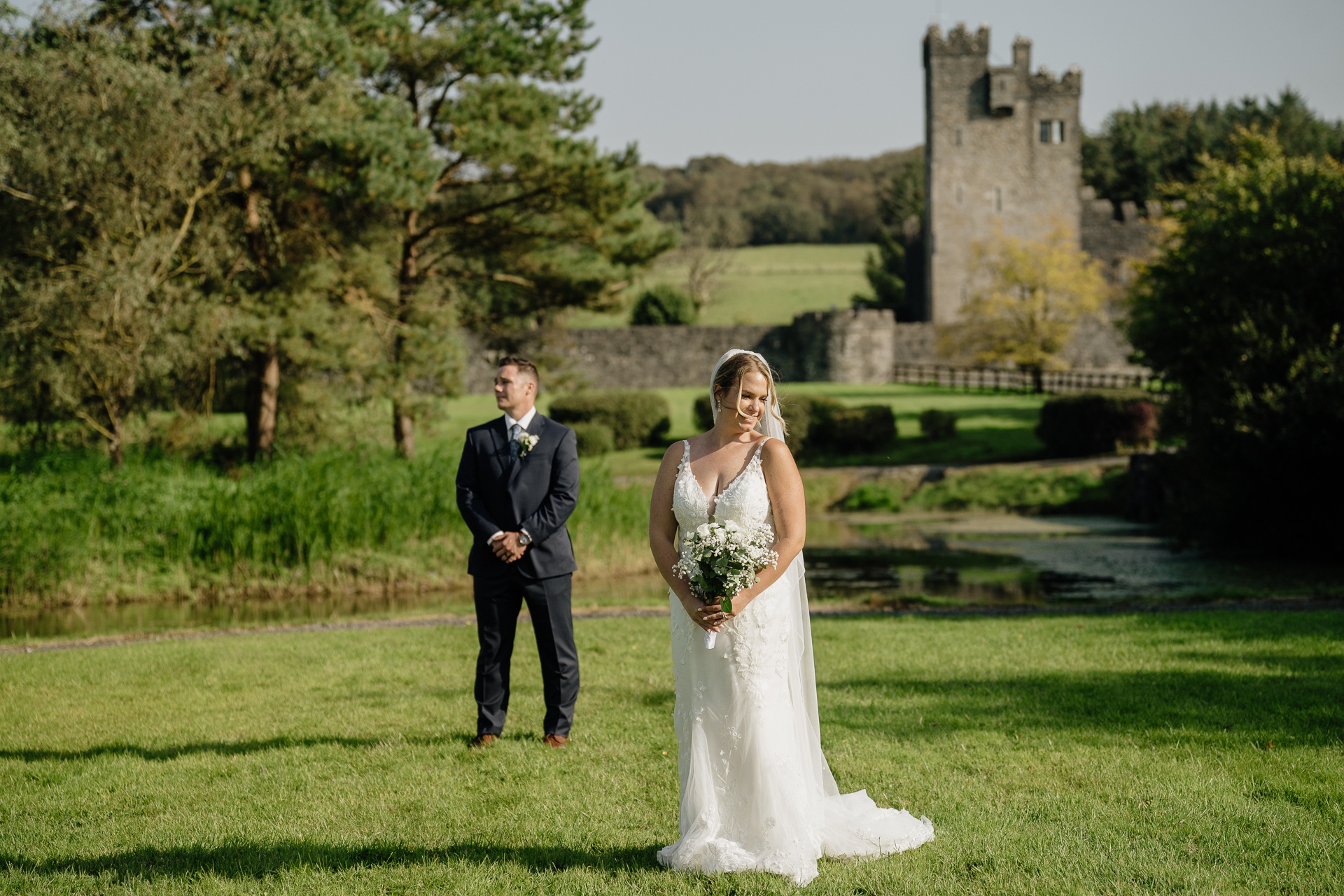 A man and woman in wedding attire walking in a grass field