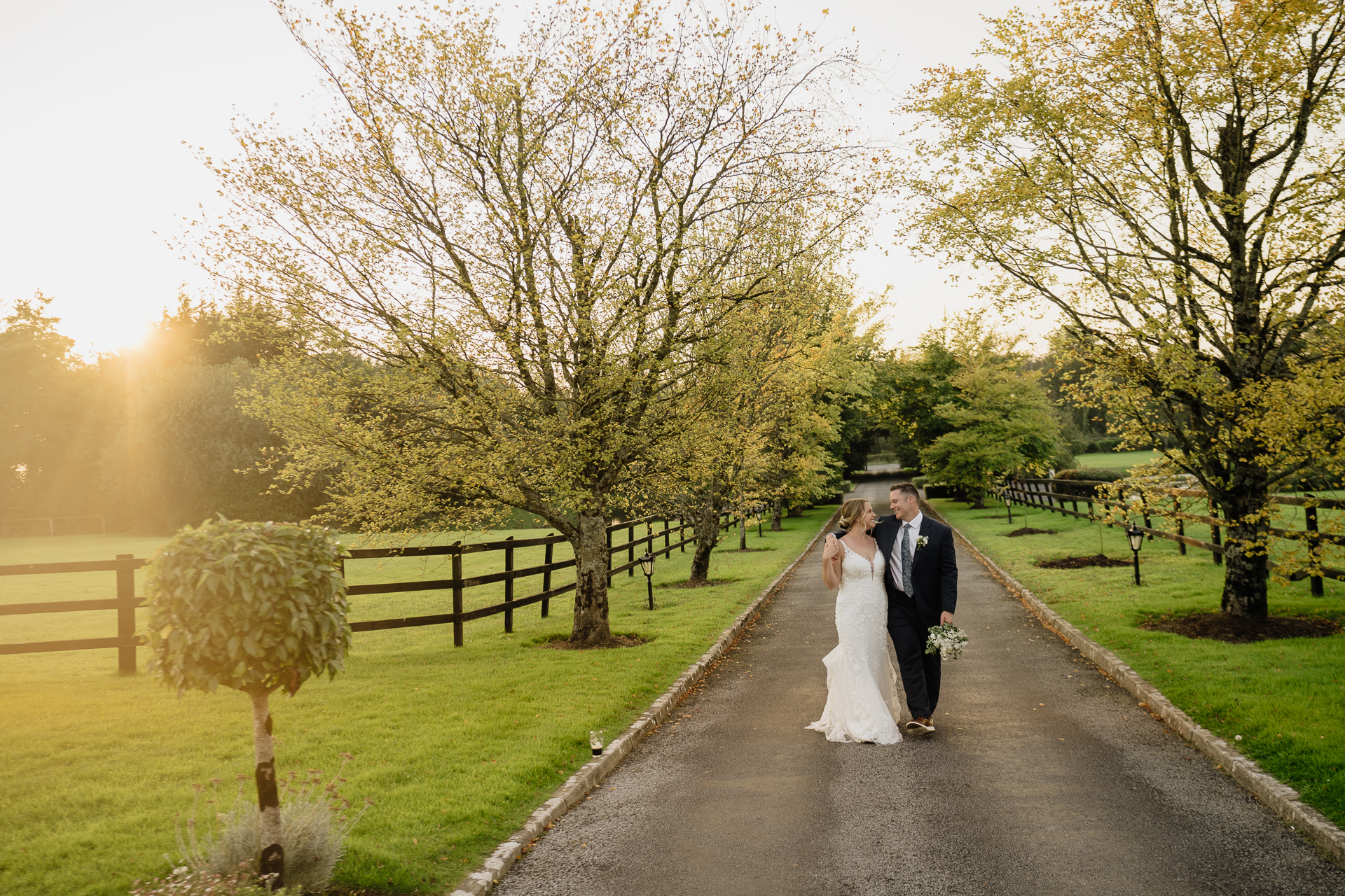 A man and woman walking down a road with trees on either side