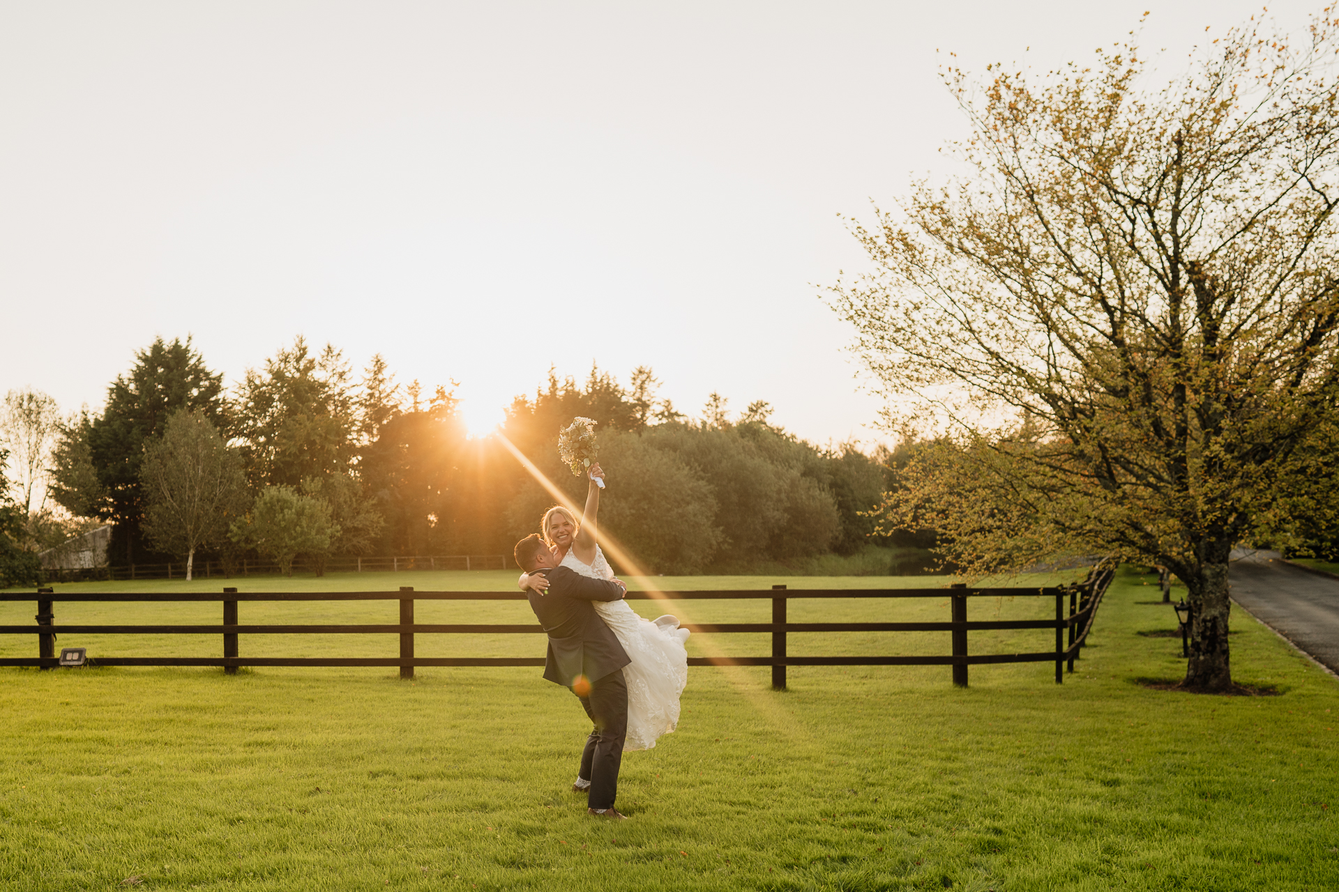 A man holding a woman in a field with trees in the background