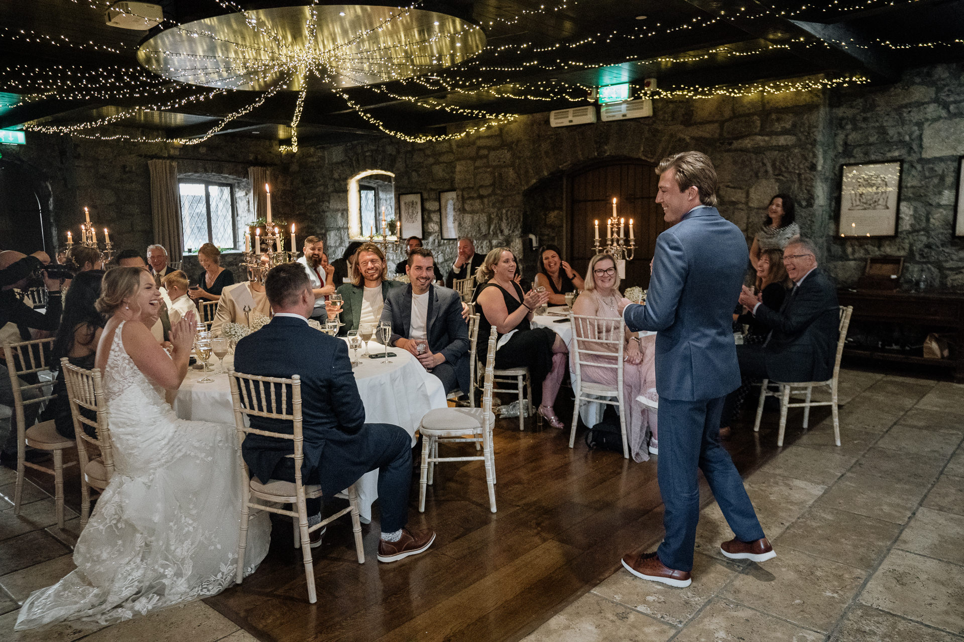 A man and woman walking down a hall with a group of people sitting at tables