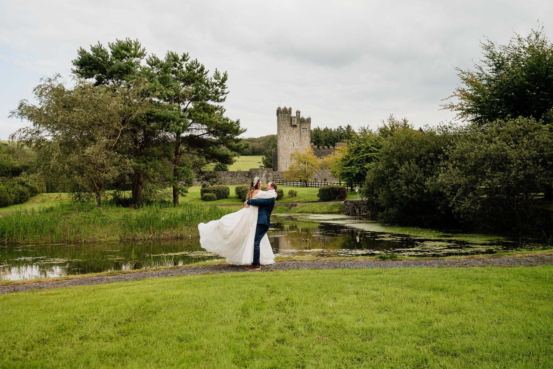 A man and woman kissing in a grass field with a castle in the background