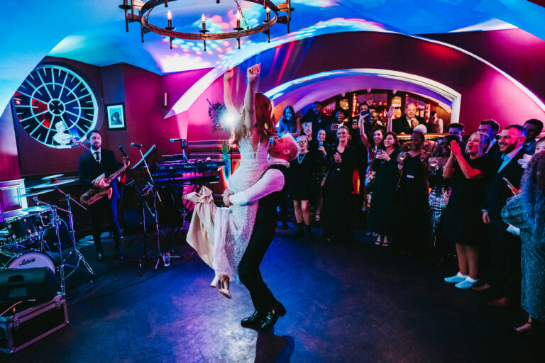 A bride and groom dancing during their wedding reception at Markree Castle with vibrant lighting and guests in the background.