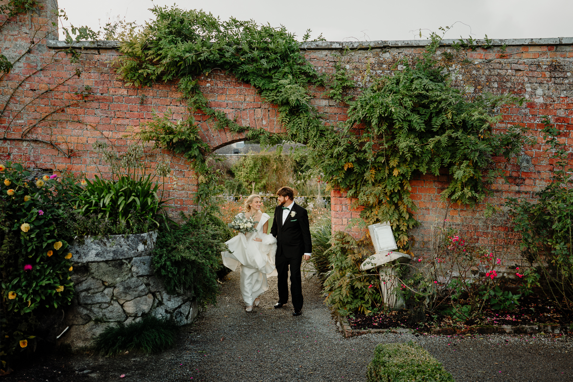 A man and woman in wedding attire standing in front of a brick wall