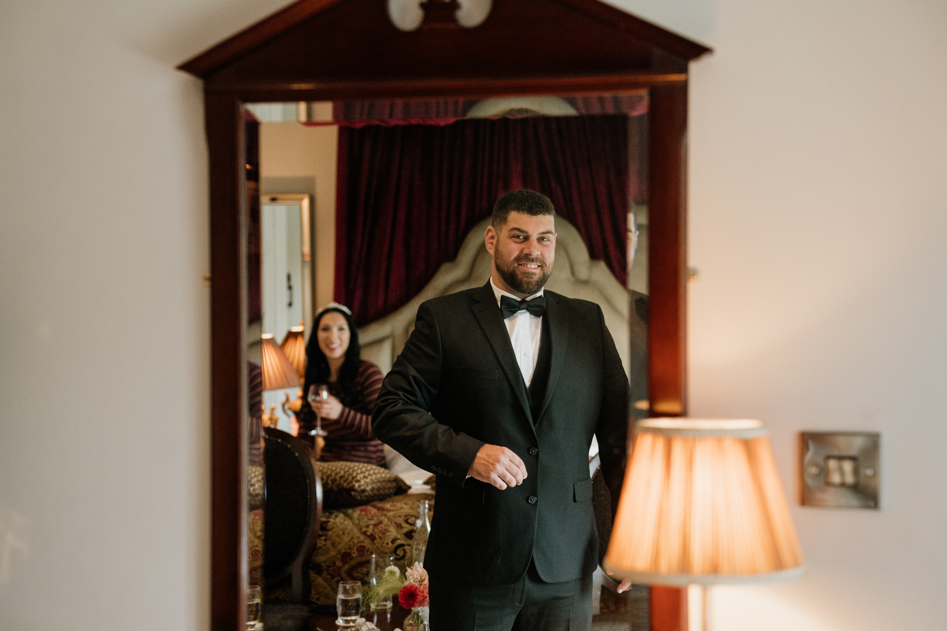 A man in a suit standing in a room with a woman in the background