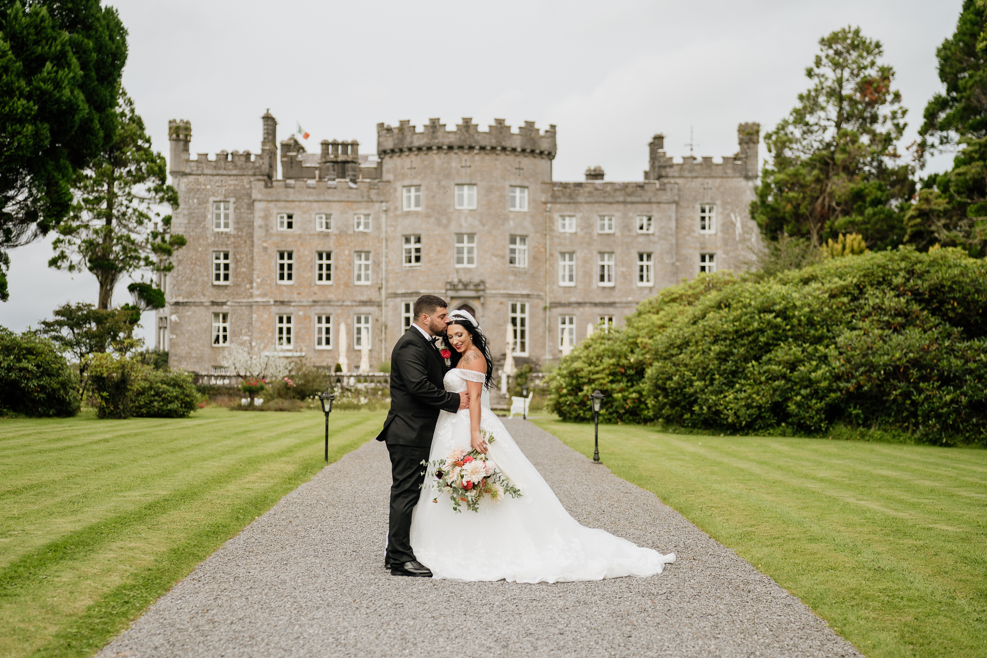 A man and woman in wedding attire kissing in front of a large building