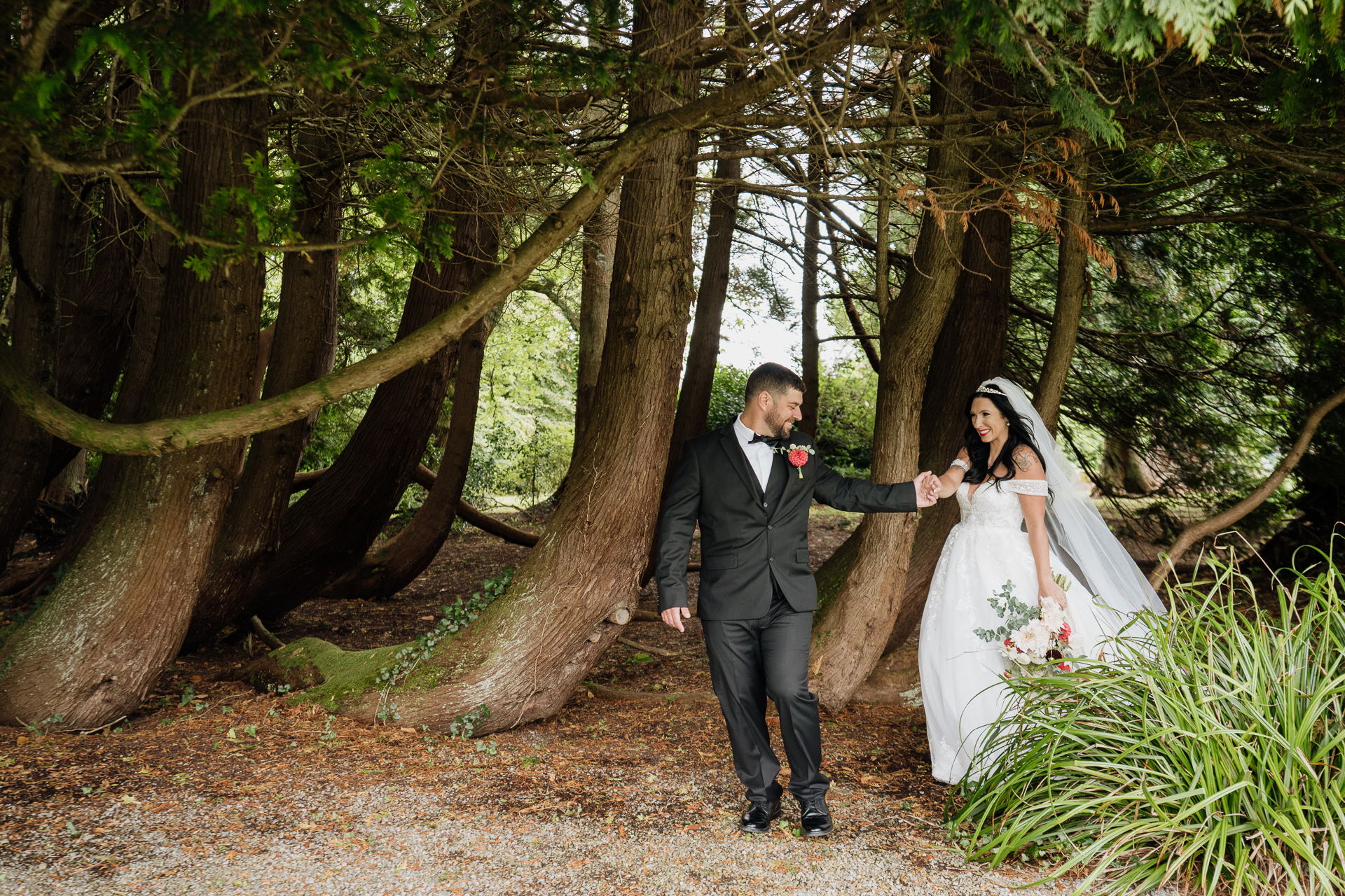 A man and woman in wedding attire walking down a path in a forest