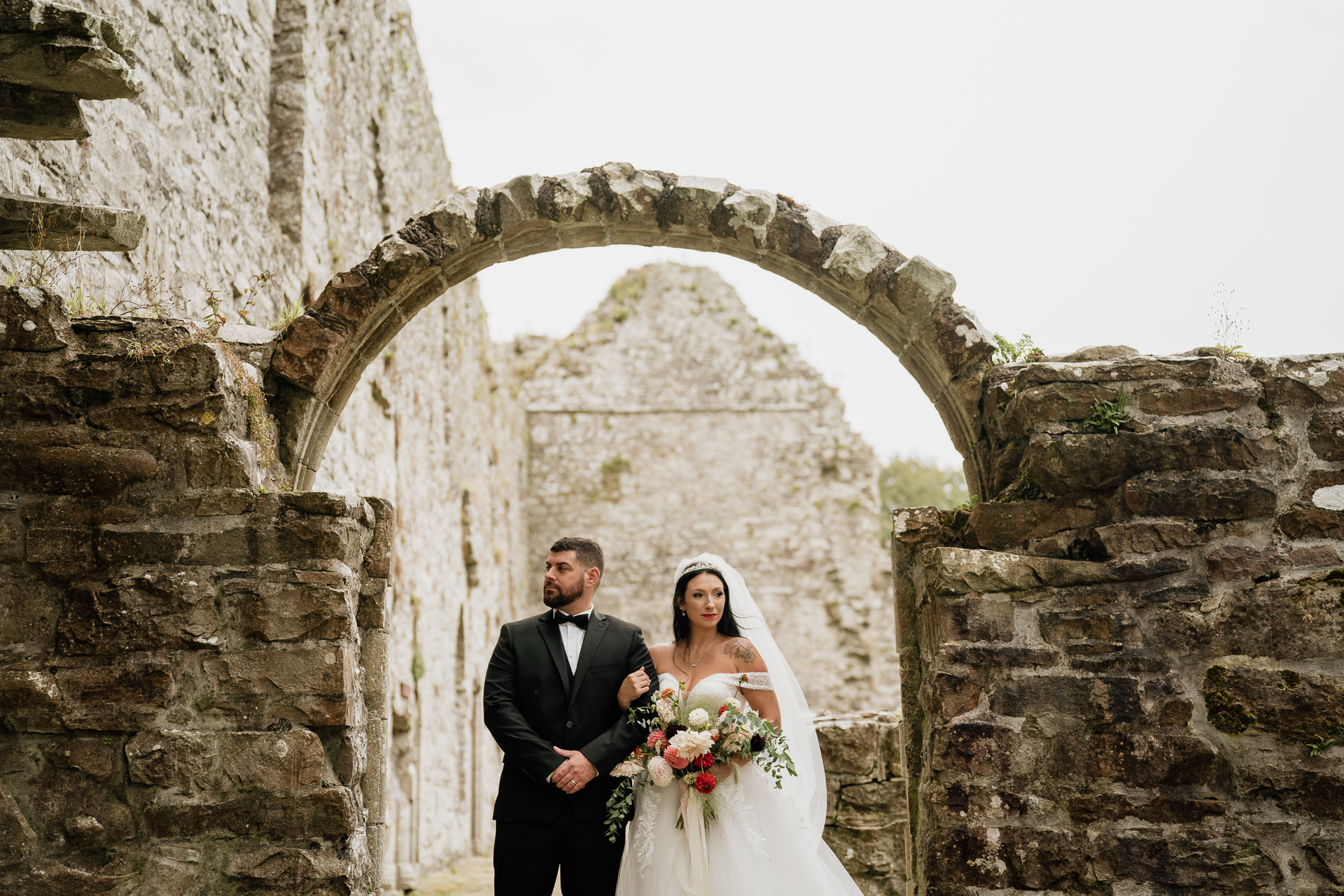 A bride and groom posing in front of a stone archway