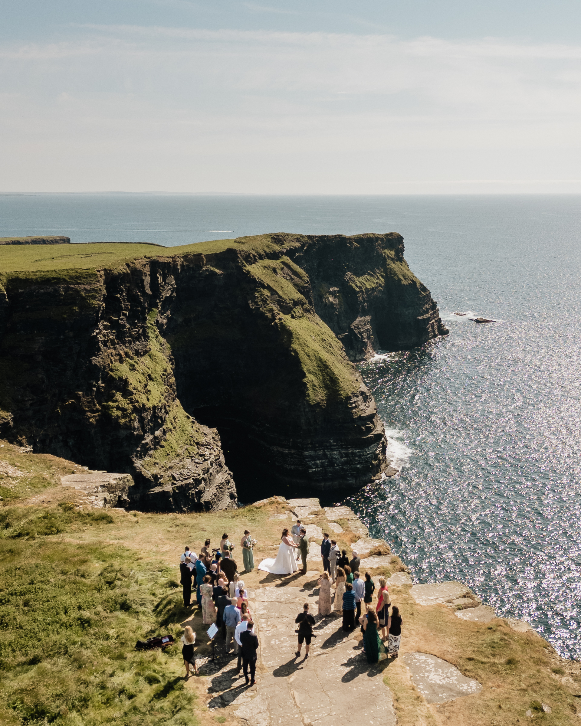 A group of people walking on a path by a body of water with Cliffs of Moher in the background