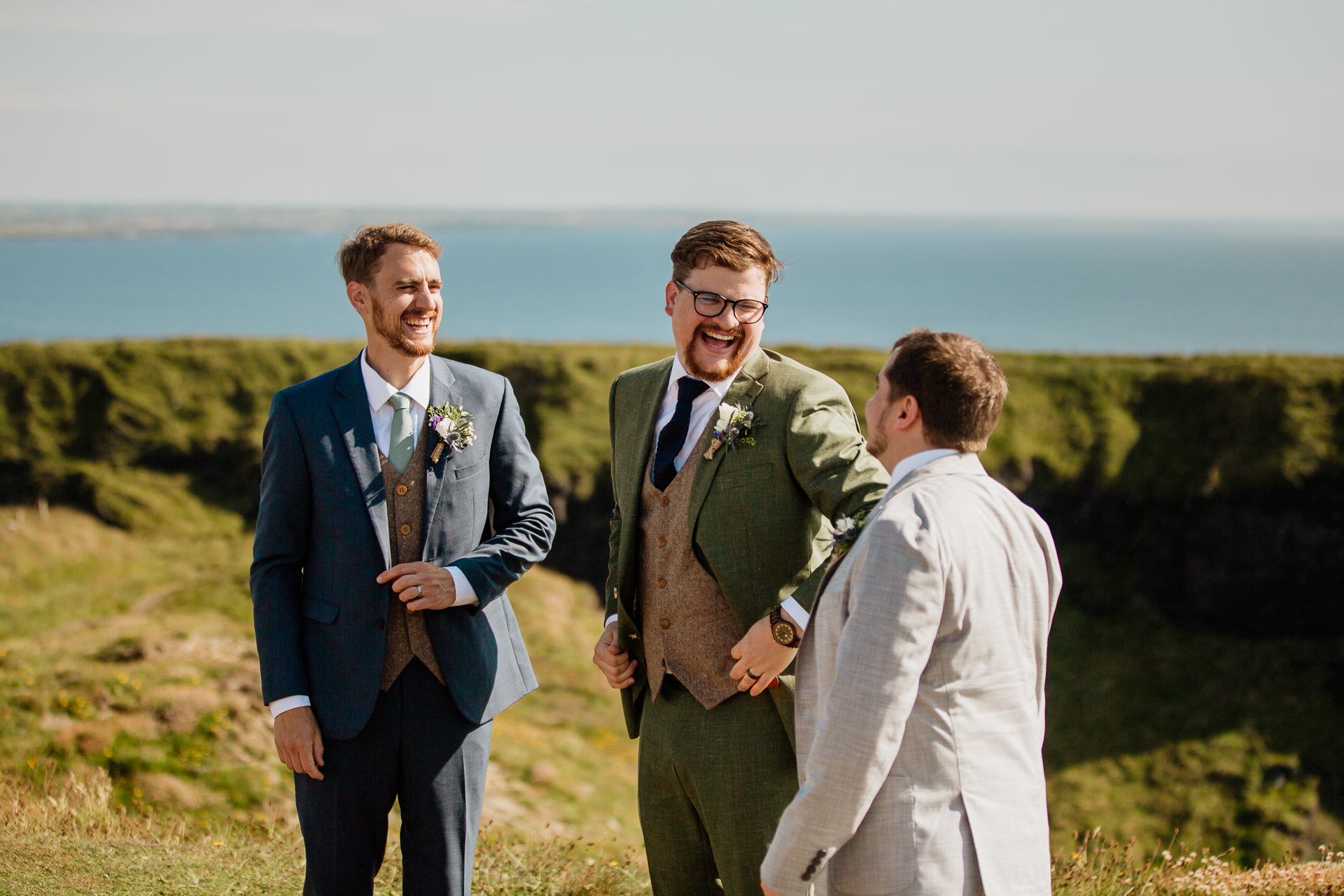 A group of men in suits standing on a hill overlooking the ocean