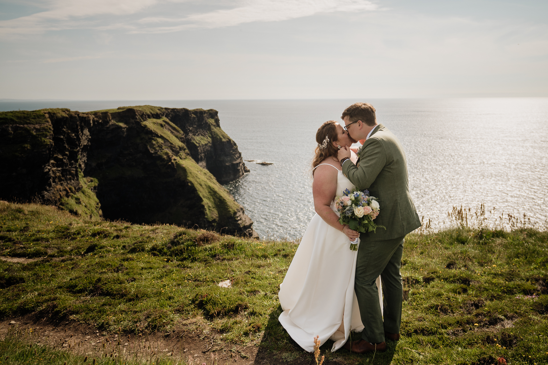 A man and woman kissing on a hill overlooking a body of water