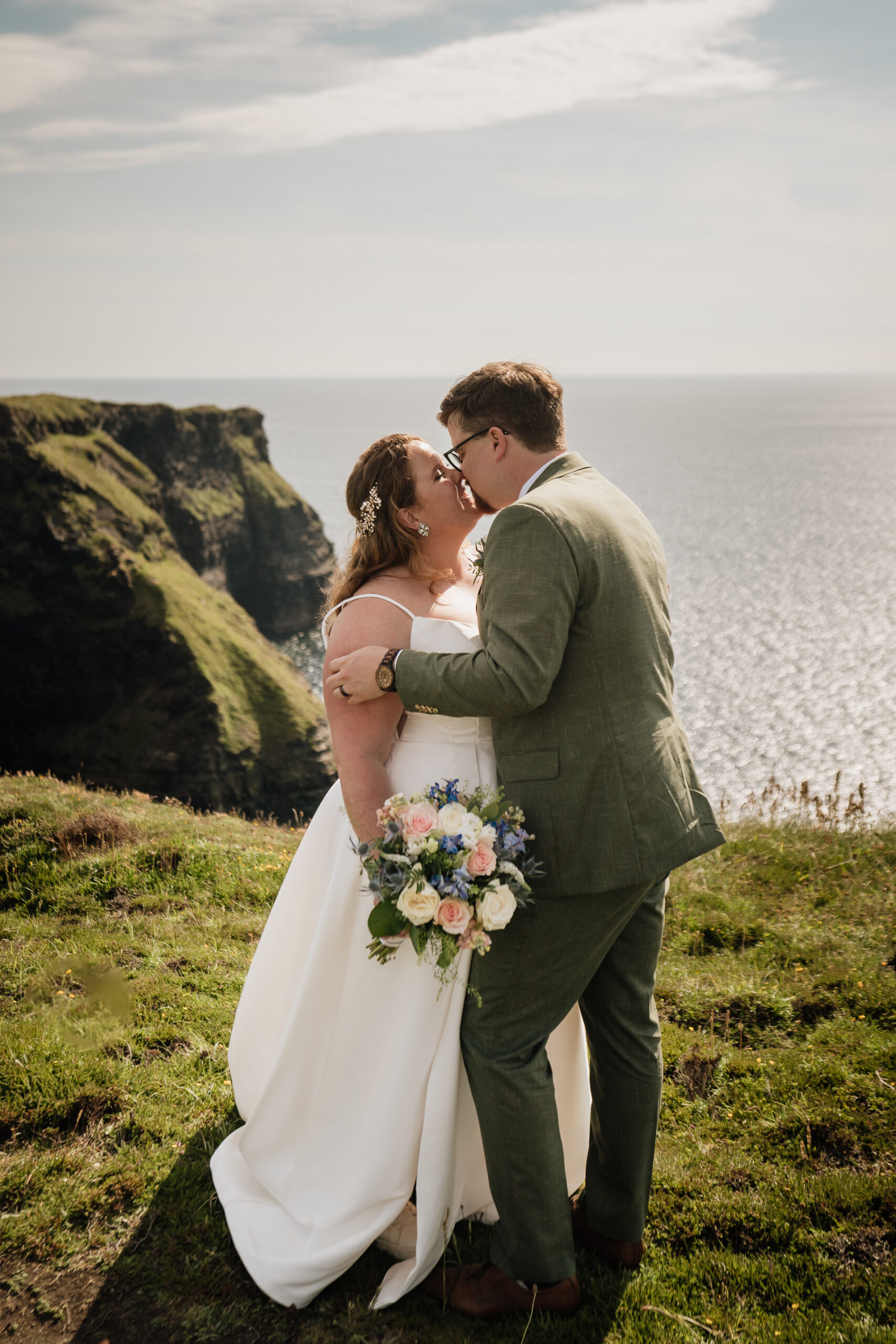 A man and woman kissing on a hill overlooking a body of water