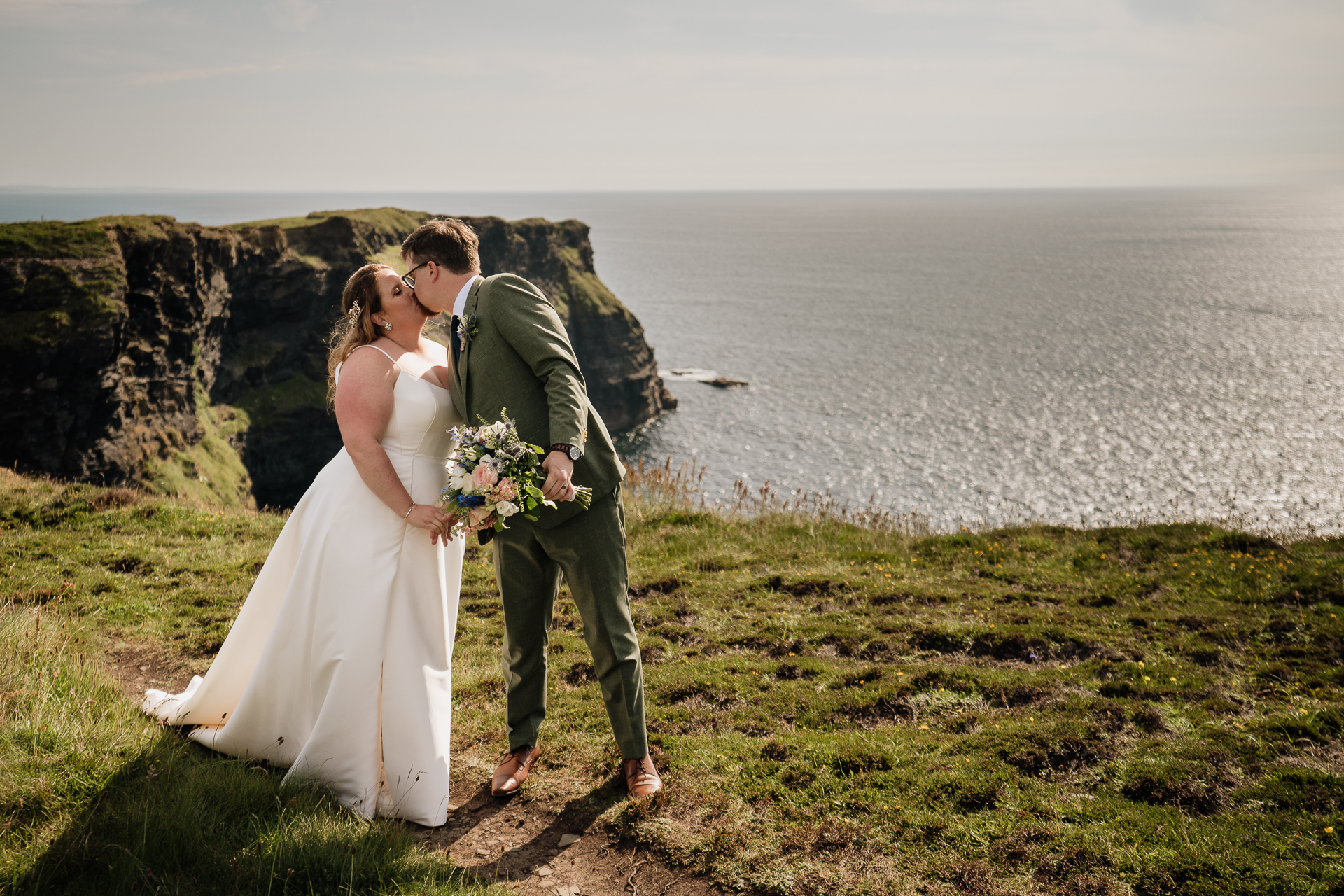 A man and woman kissing on a hill overlooking a body of water