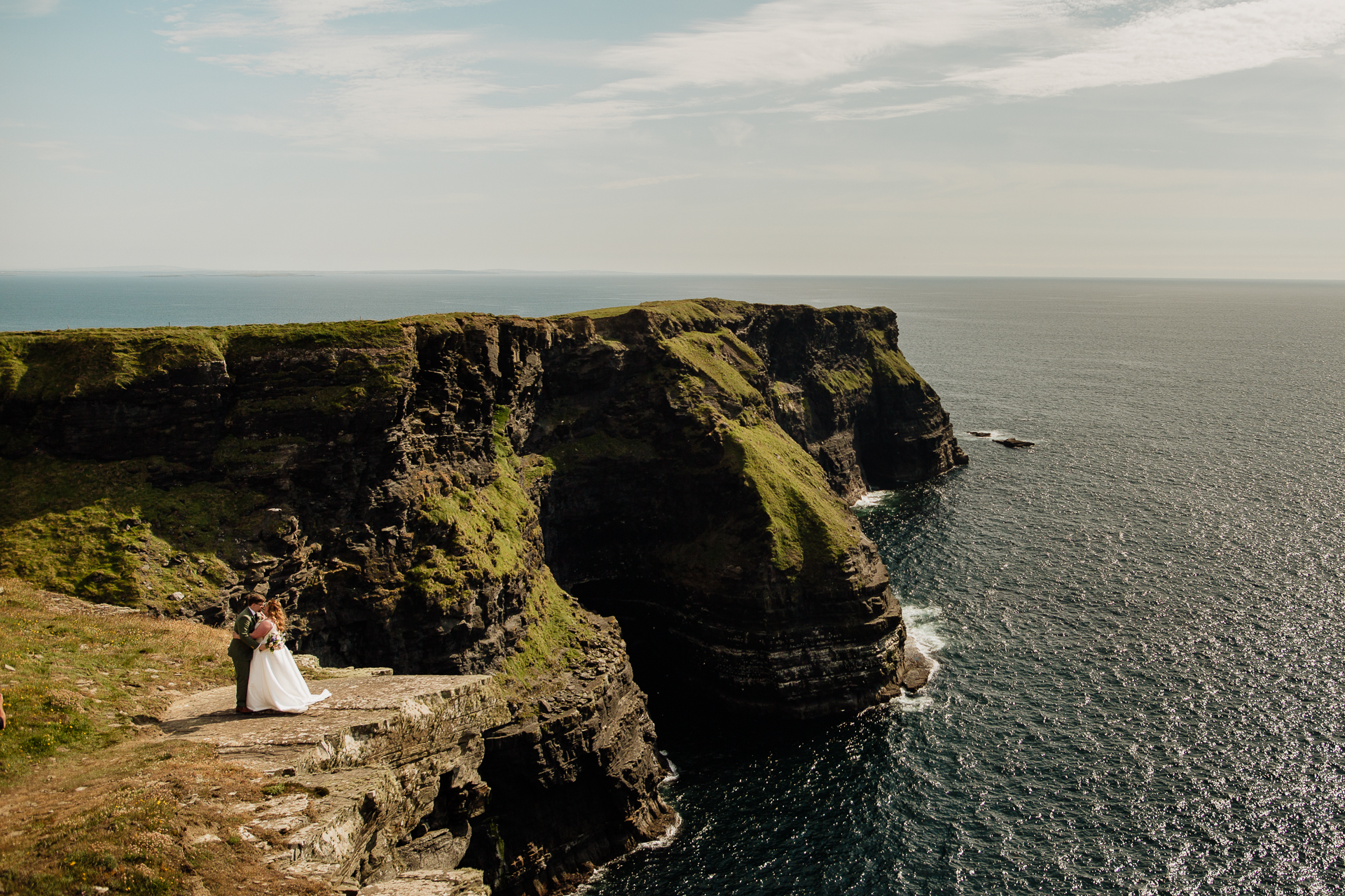 A couple people standing on a cliff overlooking the ocean with Cliffs of Moher in the background