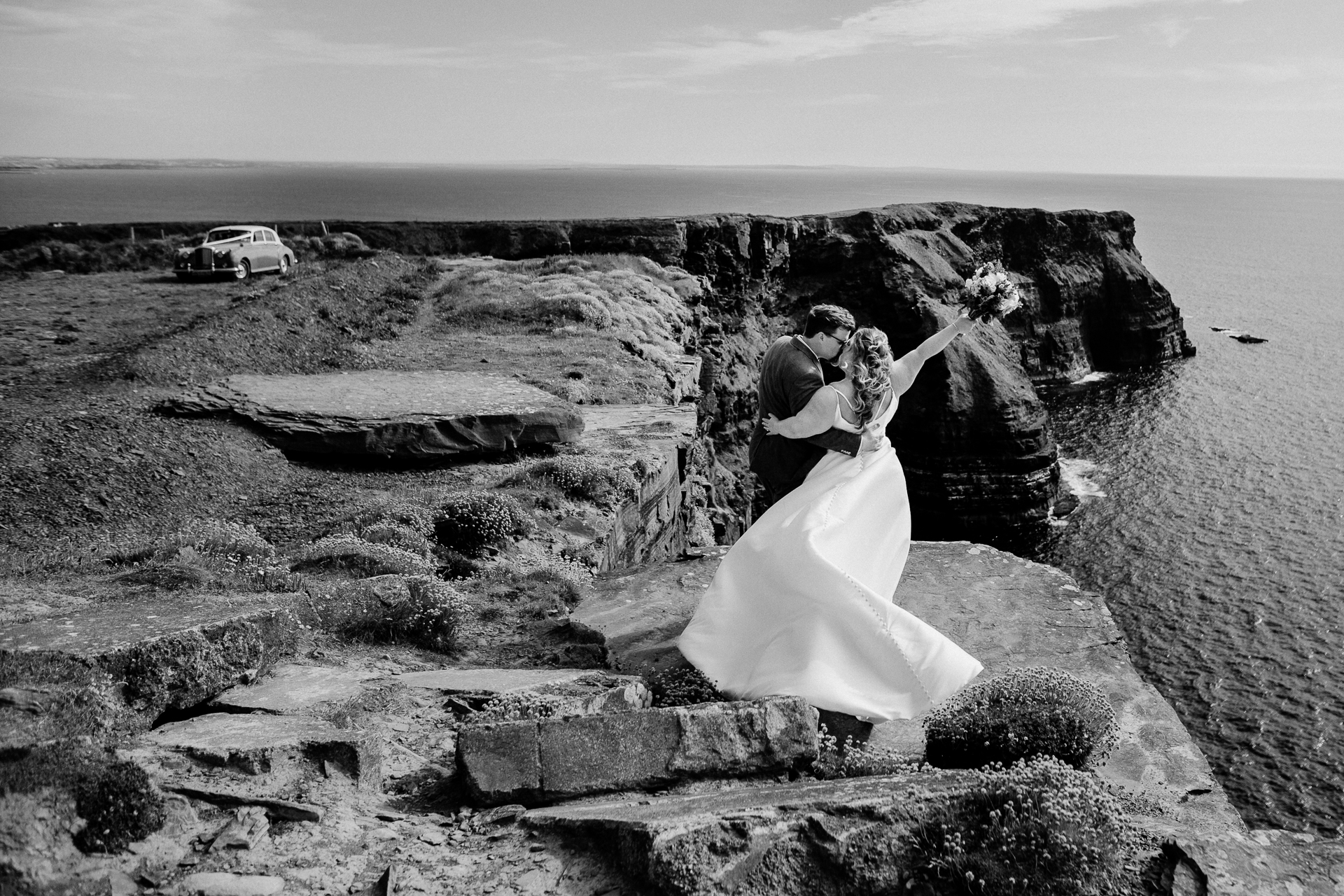 A bride and groom kissing on a rocky beach