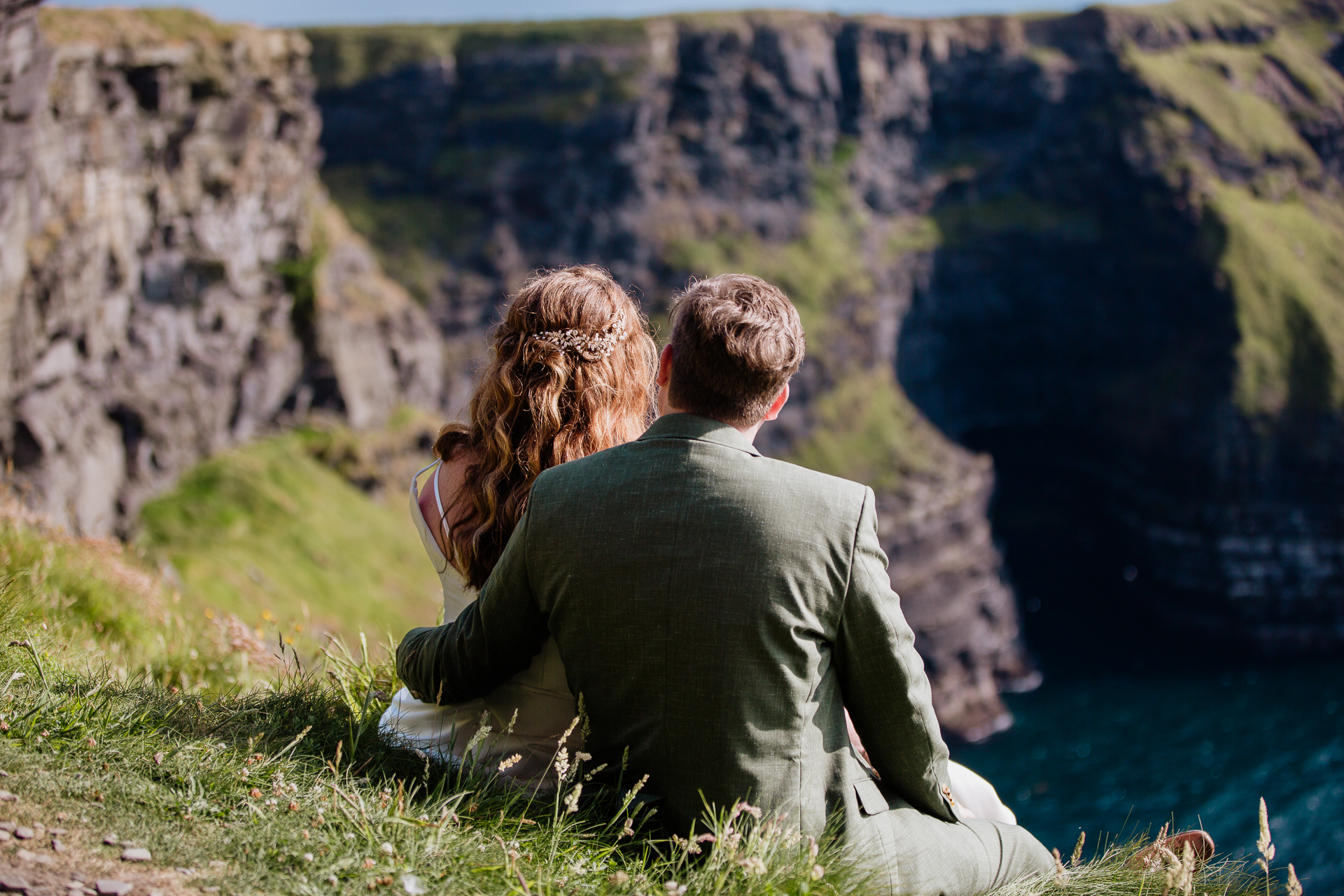 A man and woman sitting on a cliff looking at a river