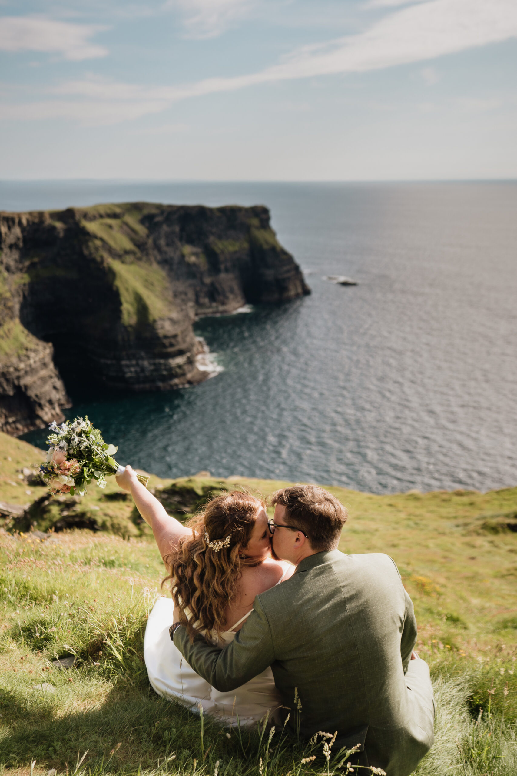 A man and woman kissing on a cliff overlooking the ocean