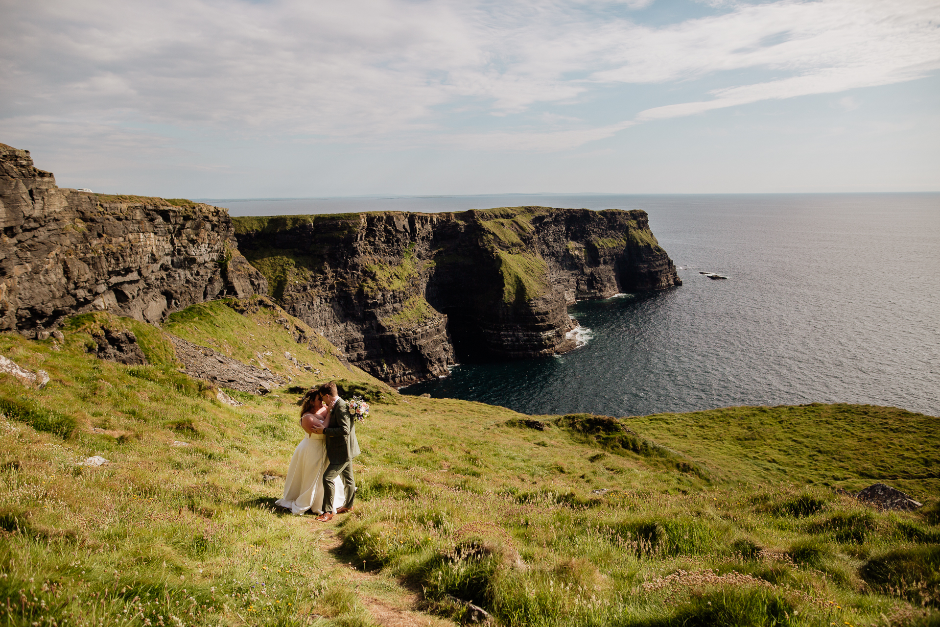 A man and woman kissing on a cliff overlooking the ocean with Cliffs of Moher in the background