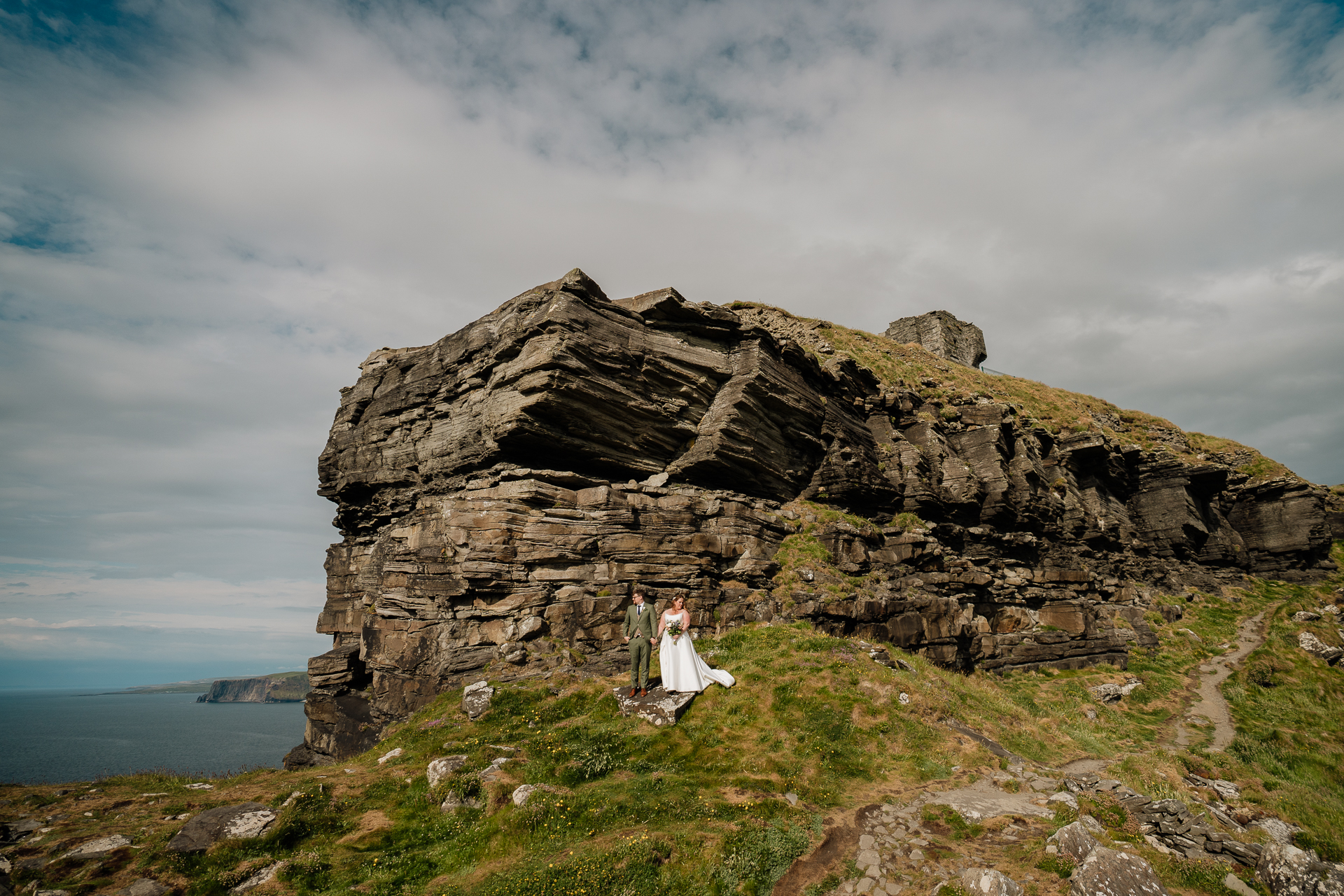 A group of people in white standing on a cliff by the water