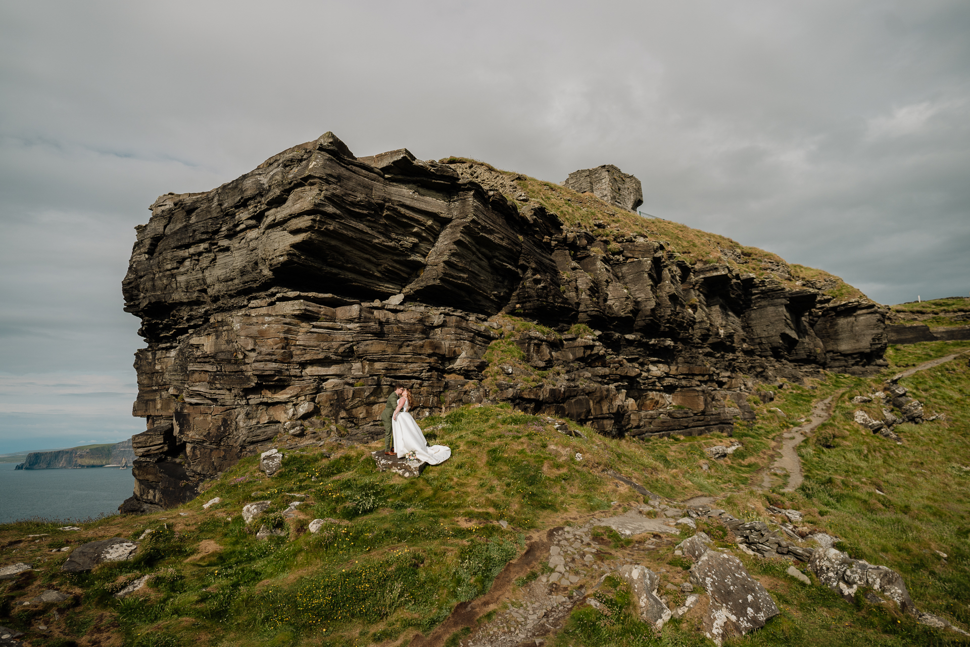 A person in a white dress sitting on a rock with a body of water in the background