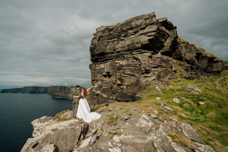 A man and woman standing on a rock by the water