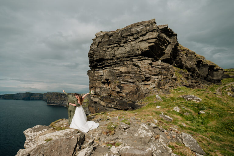 A bride and groom standing on a cliff by the water