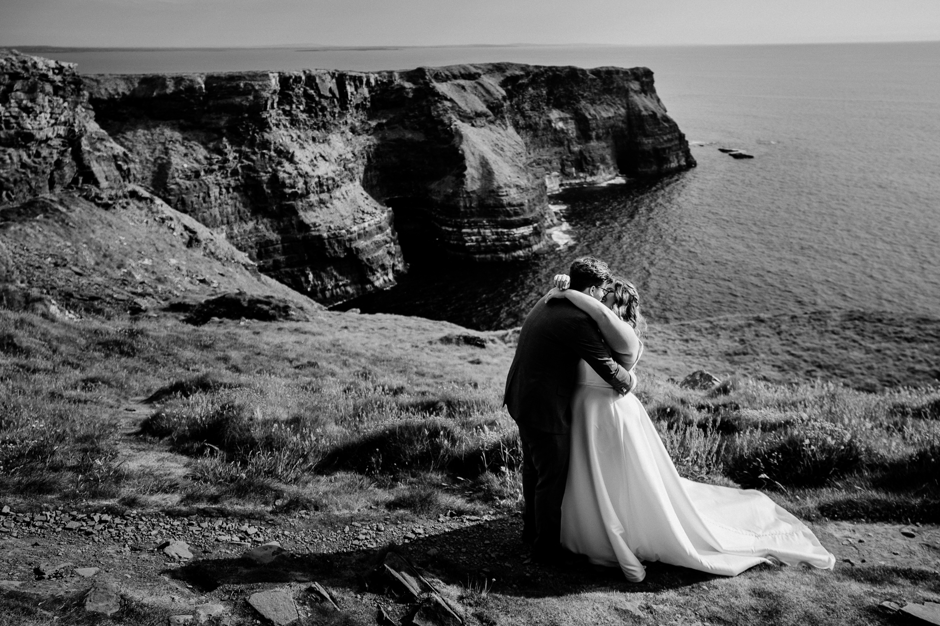 A bride and groom kissing on a cliff by the ocean