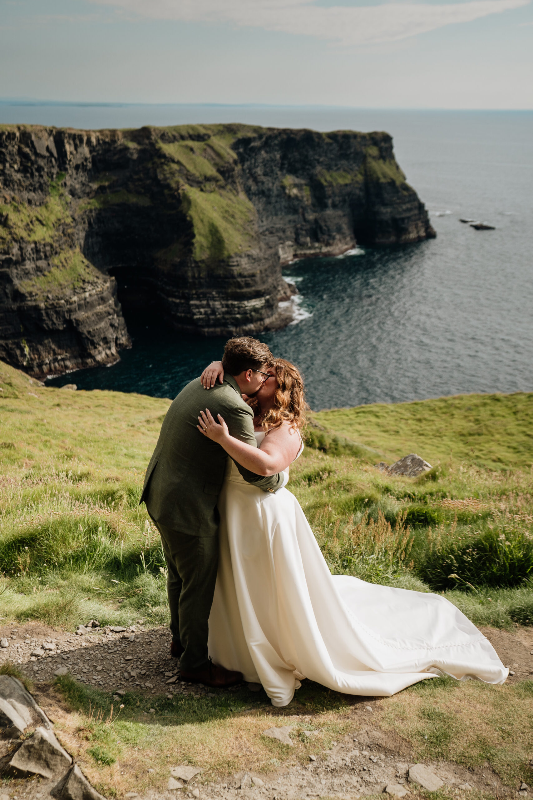 A man and woman kissing on a cliff by the water