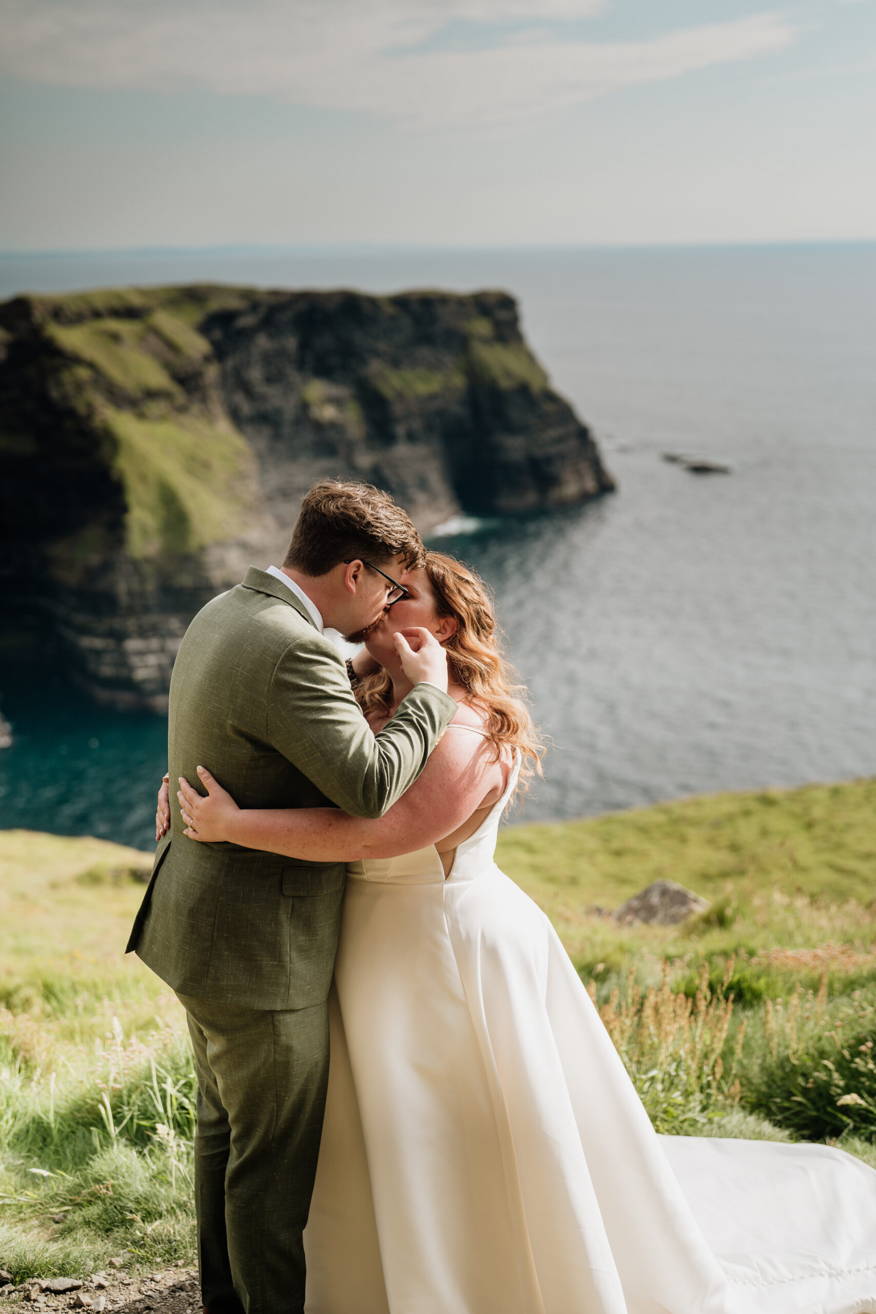 A man and woman kissing on a cliff overlooking the ocean