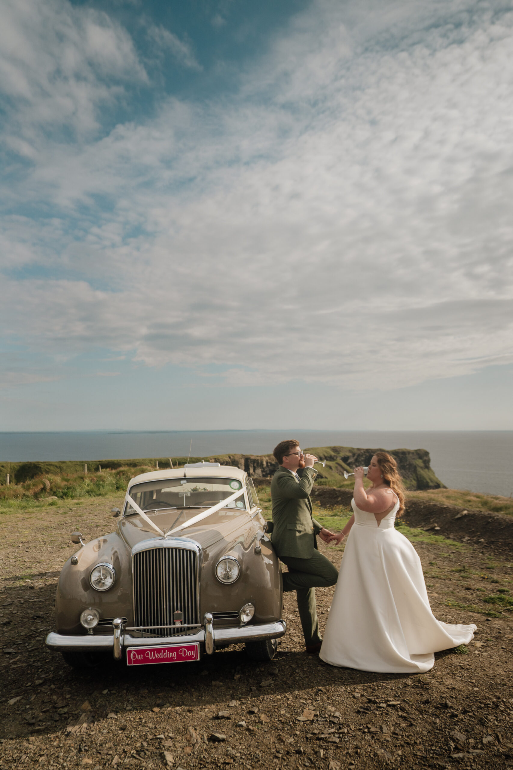 A bride and groom kissing by a car on a beach