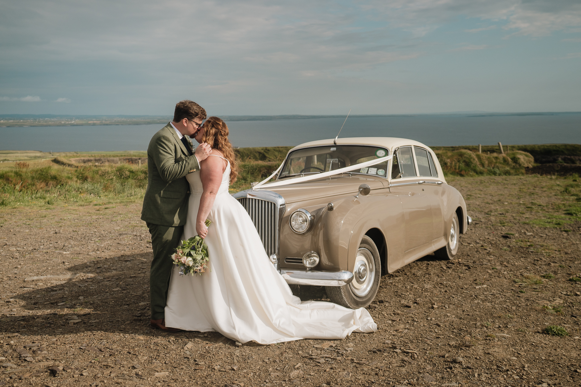 A man and woman kissing by a car on a beach