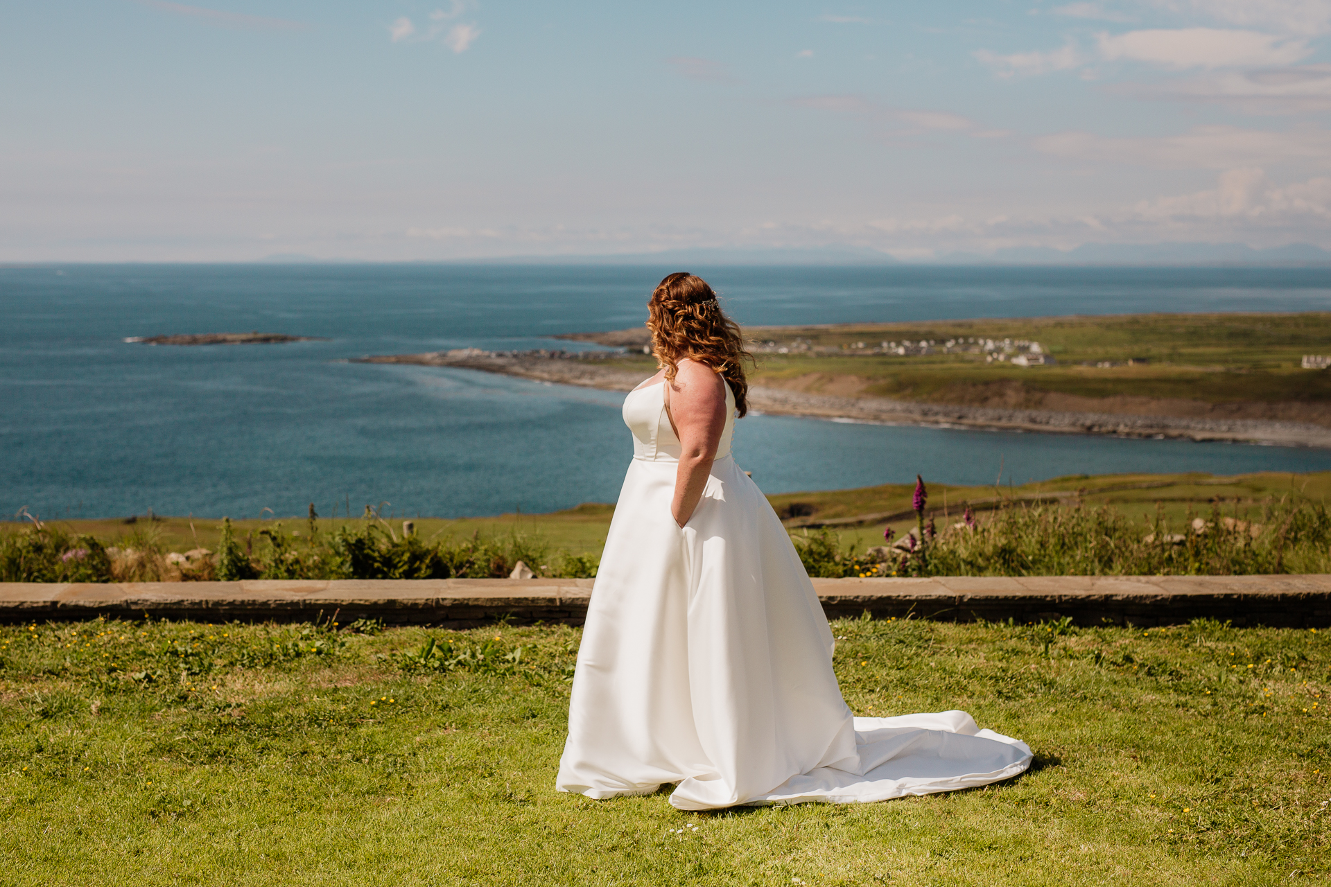 A woman in a white dress sitting on a ledge overlooking a body of water