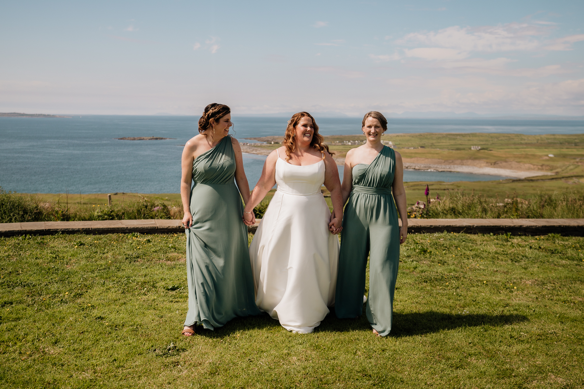 A group of women in dresses standing on grass by a body of water