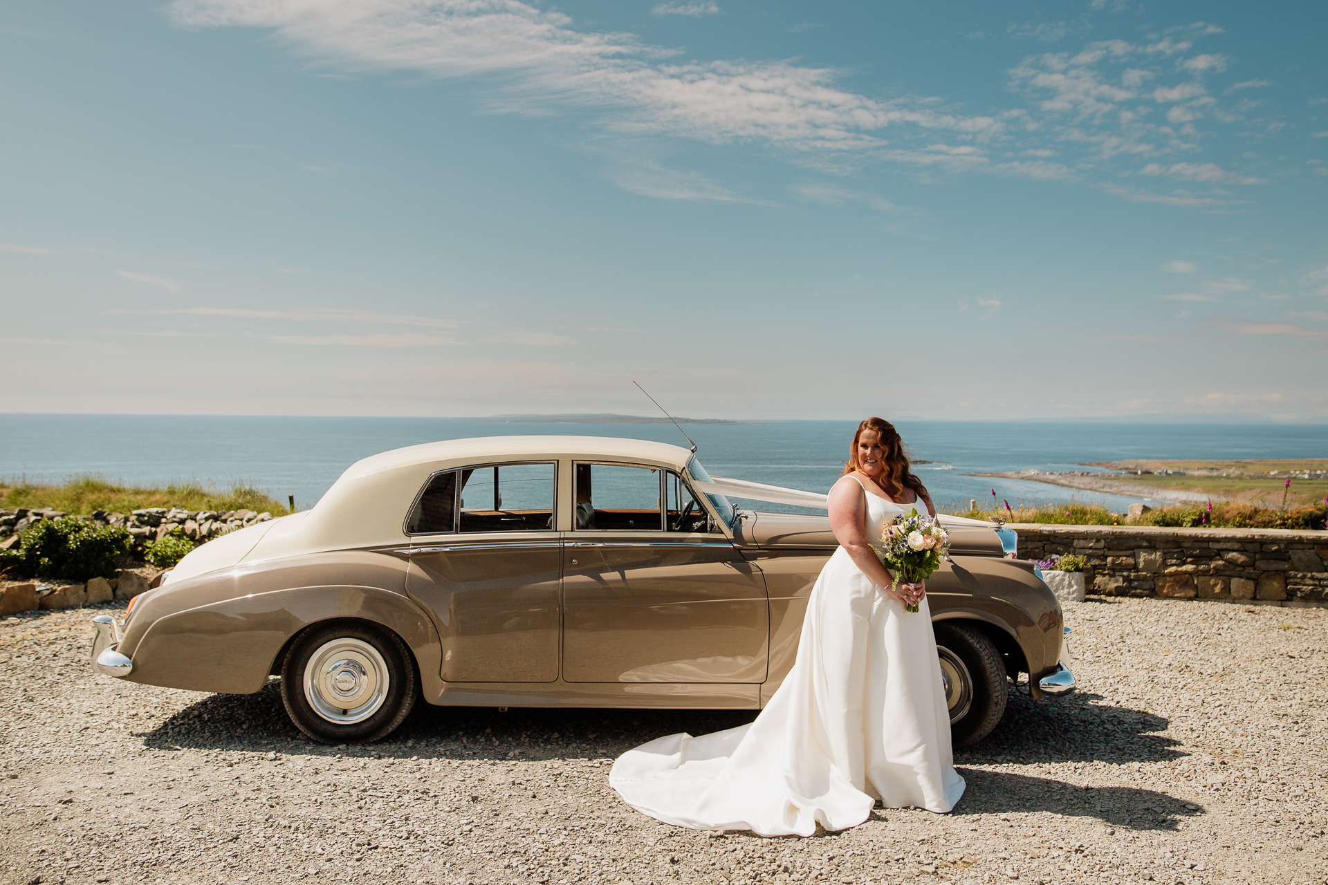 A person in a wedding dress standing next to a car on a beach