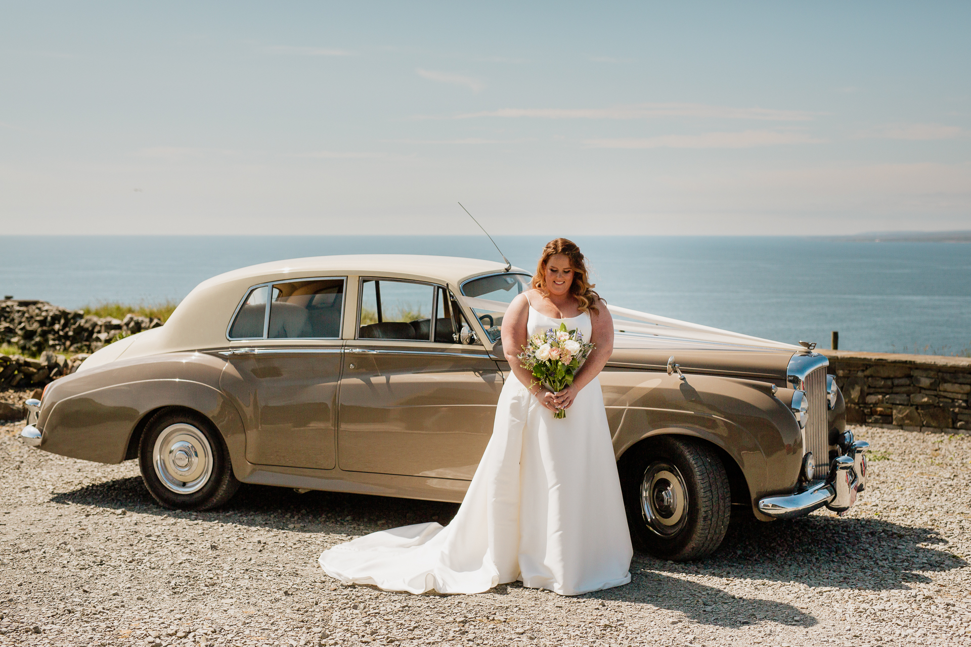 A person in a wedding dress standing next to a car on a beach