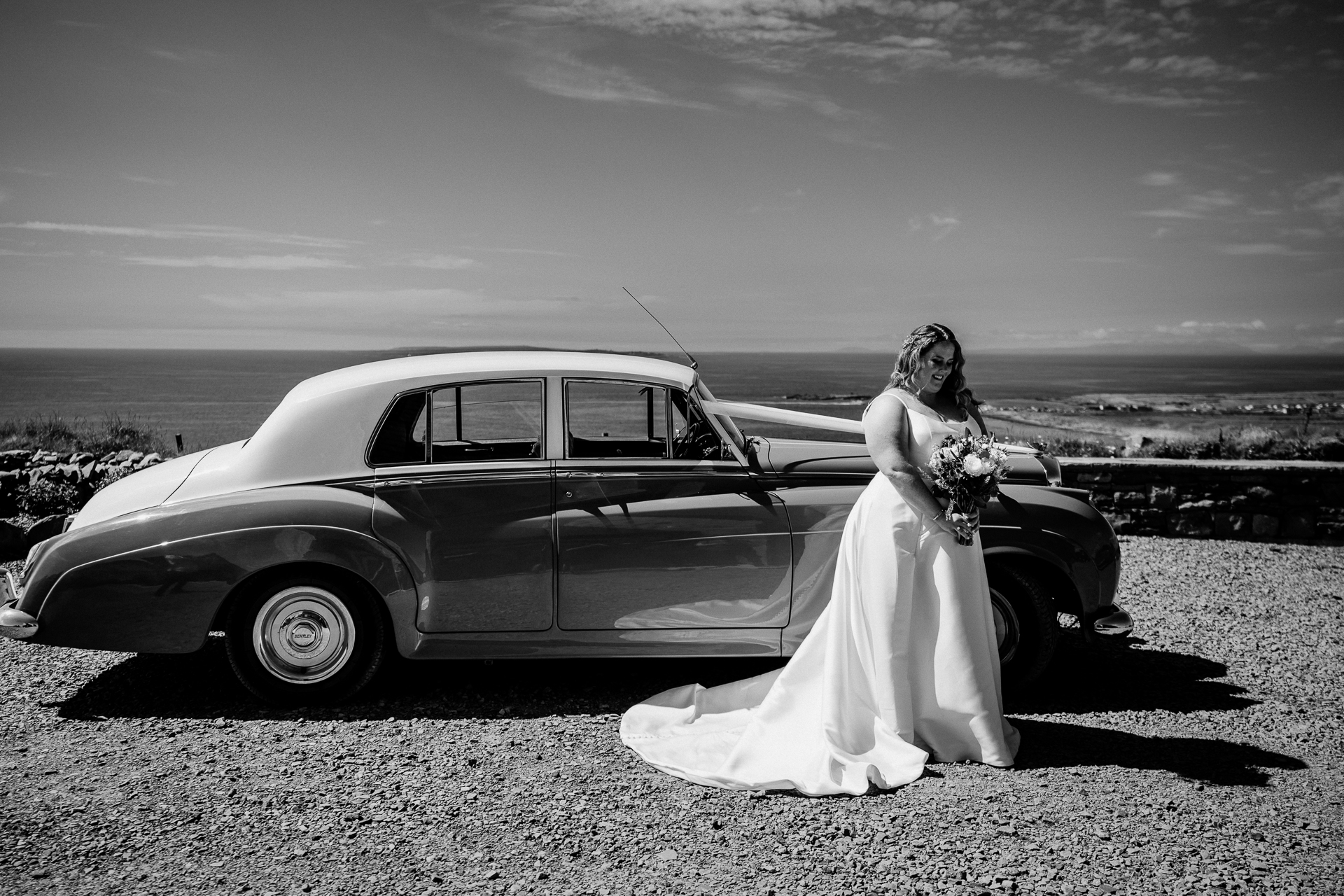 A bride and groom posing by a car on a beach