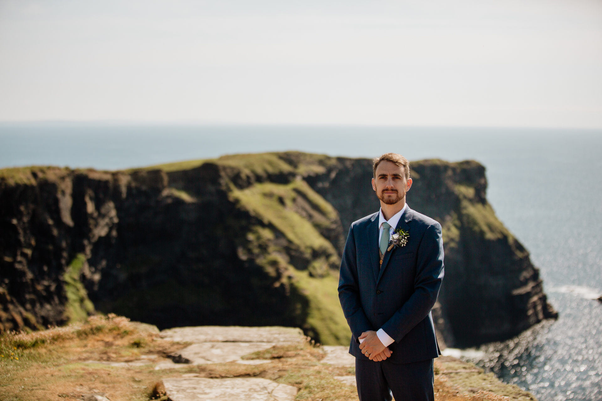 A man in a suit standing on a cliff overlooking the ocean