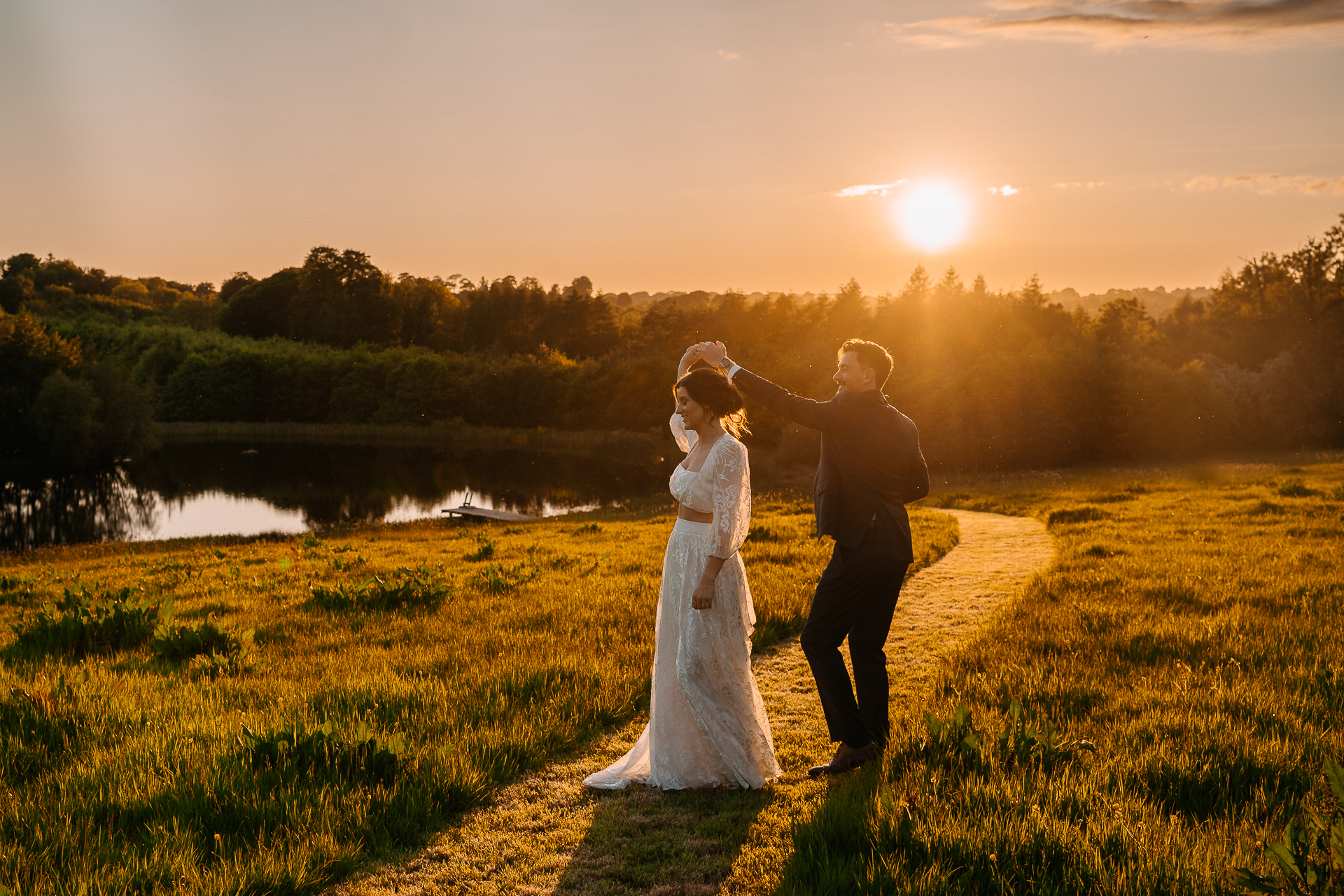 A man and woman kissing in a field with a body of water in the background