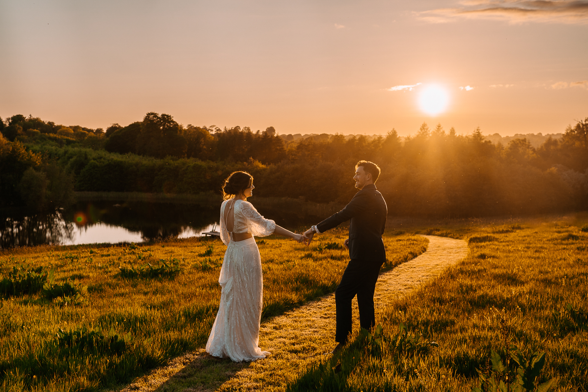 A man and woman holding hands in a field with a body of water in the background