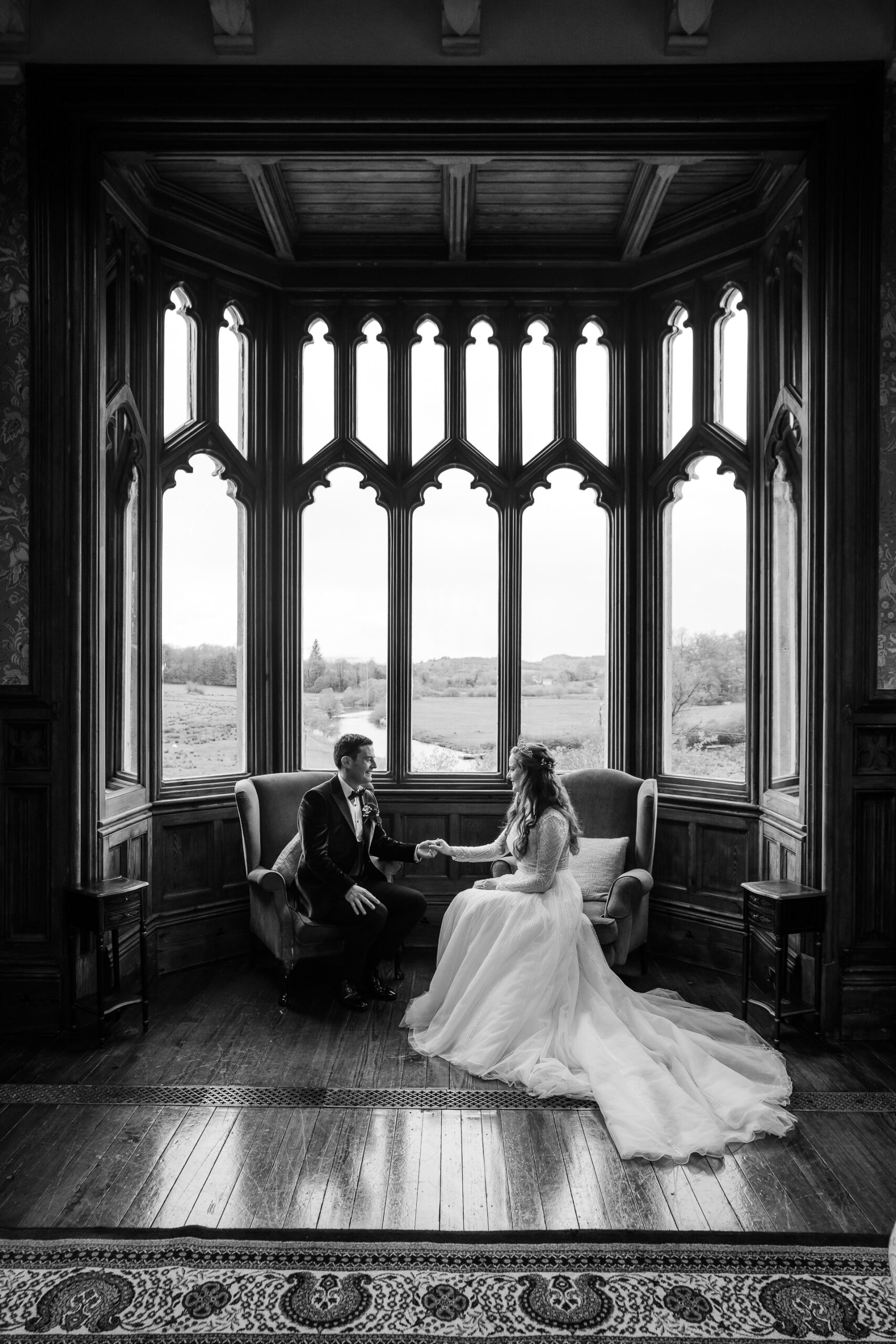 A bride and groom sitting in a room with large windows