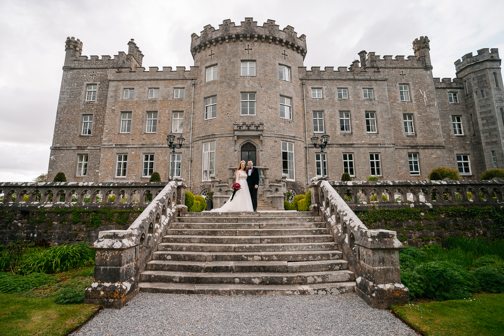 A bride and groom on stairs in front of a large brick building