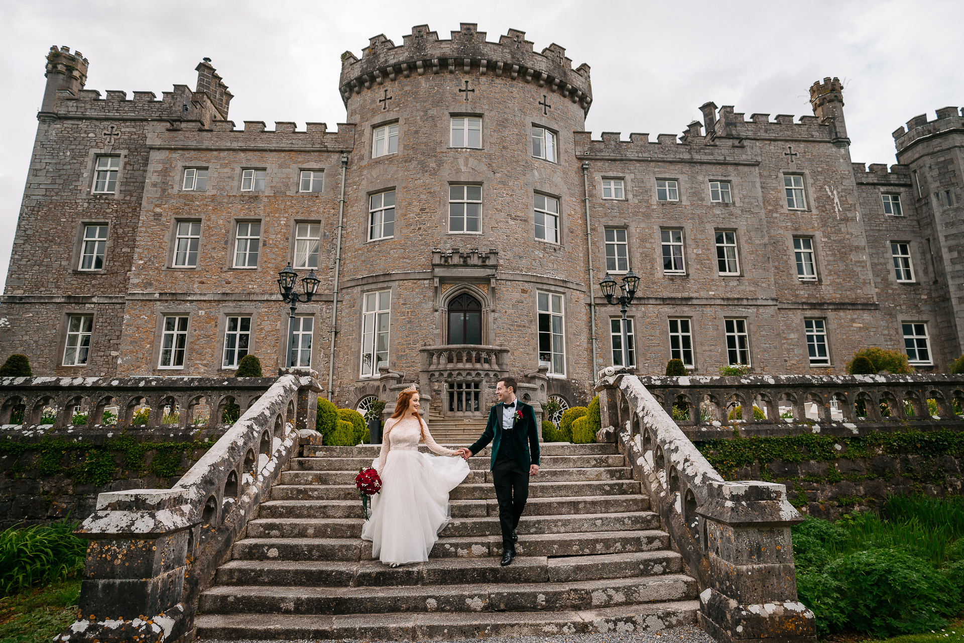 A man and woman in wedding attire walking up stairs to a large brick building