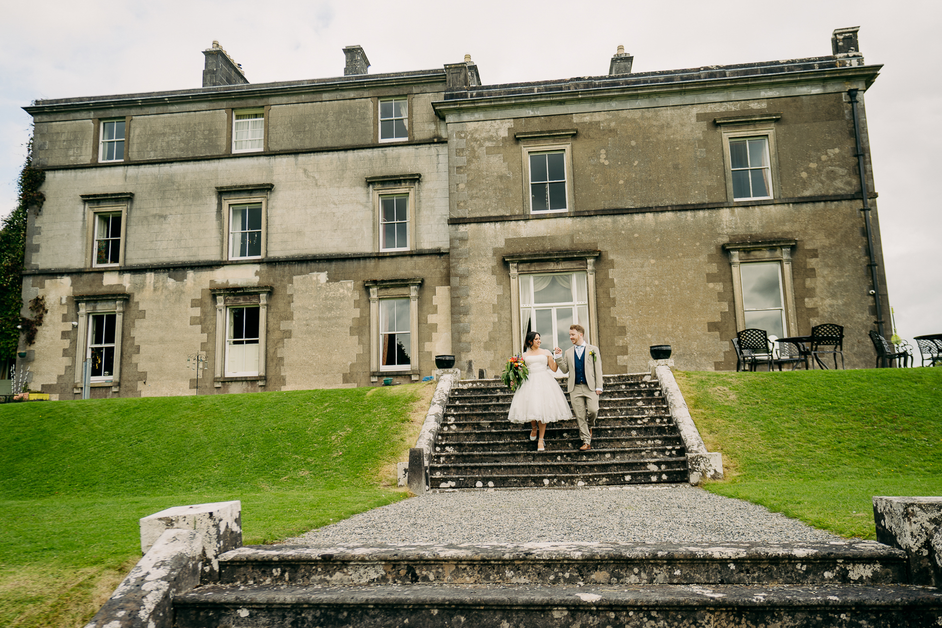 A bride and groom on steps in front of a large stone building