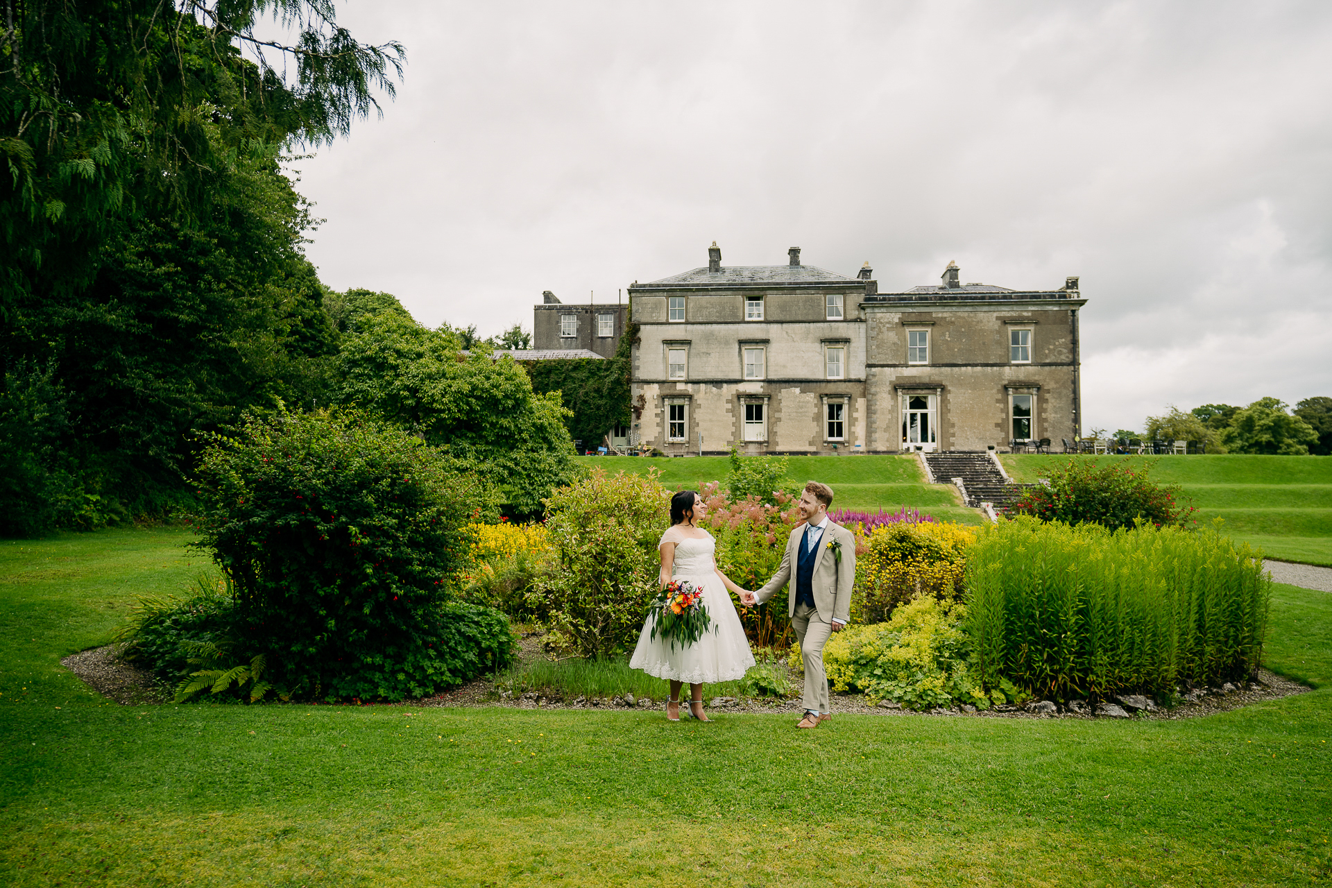 A man and woman walking in a garden in front of a large building