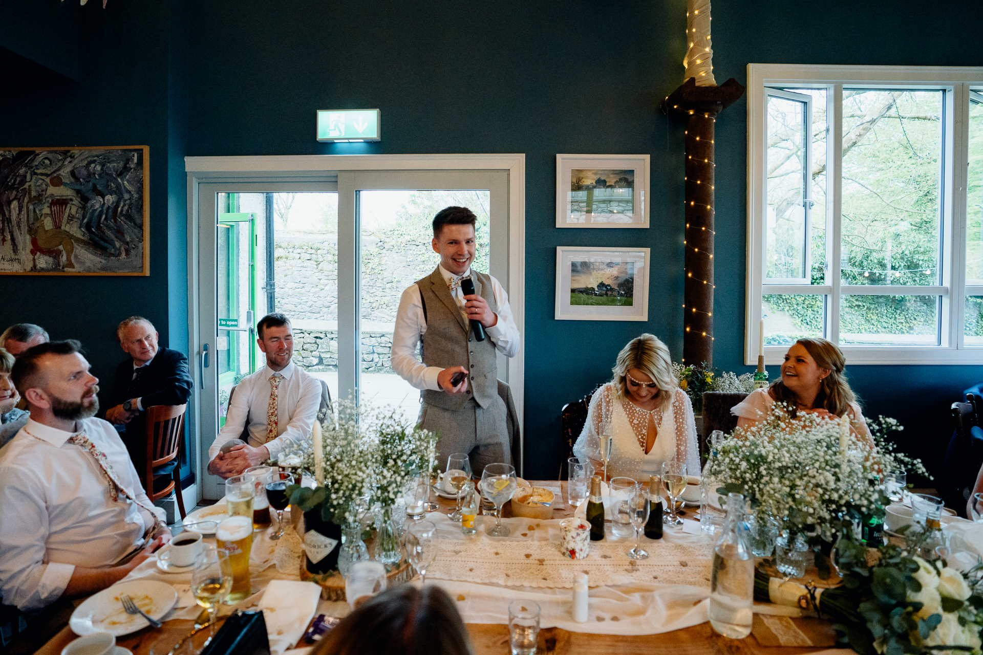 A person in a suit standing in front of a table with people sitting around it