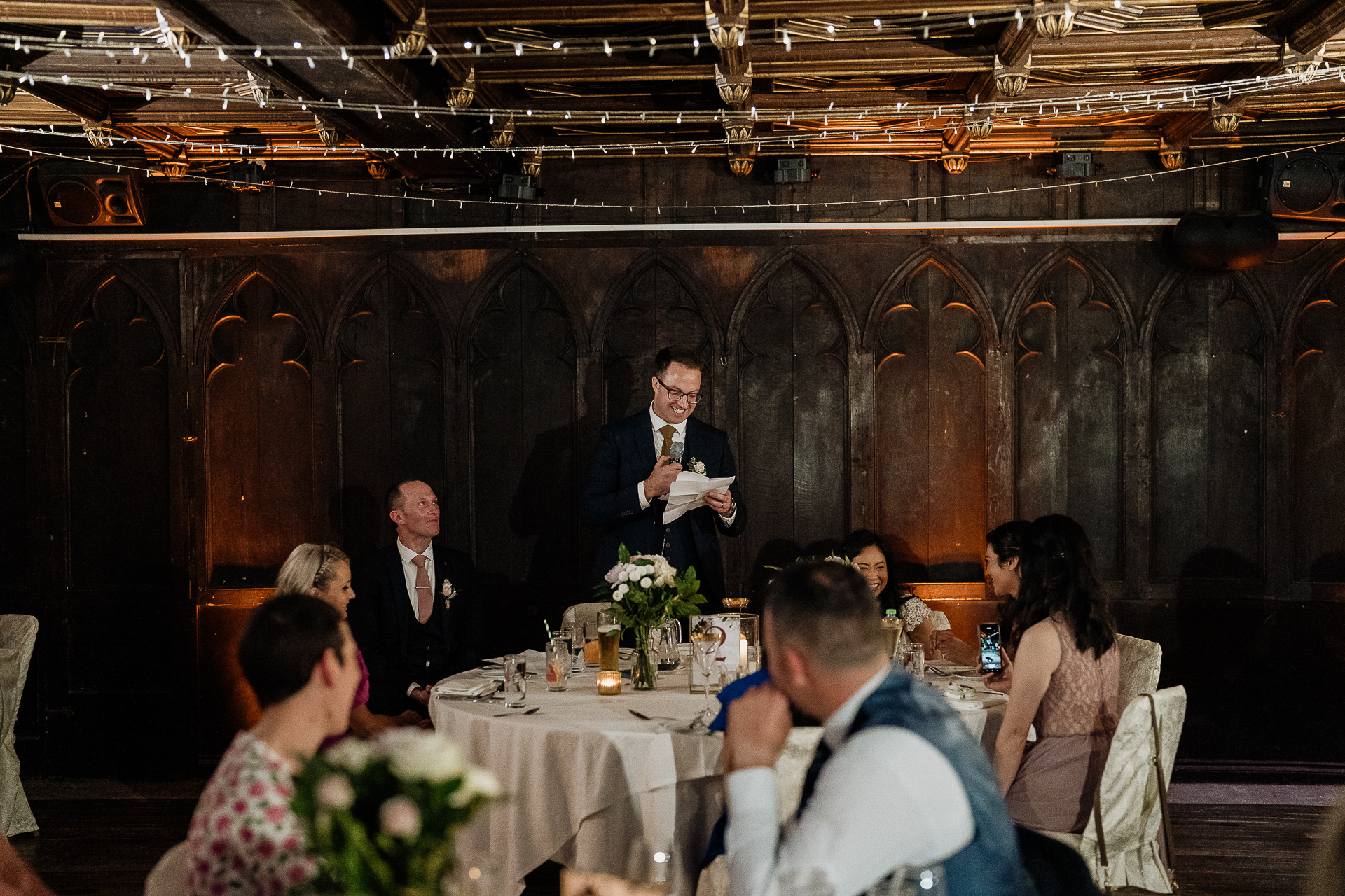 A person in a suit and tie standing in front of a group of people sitting at tables